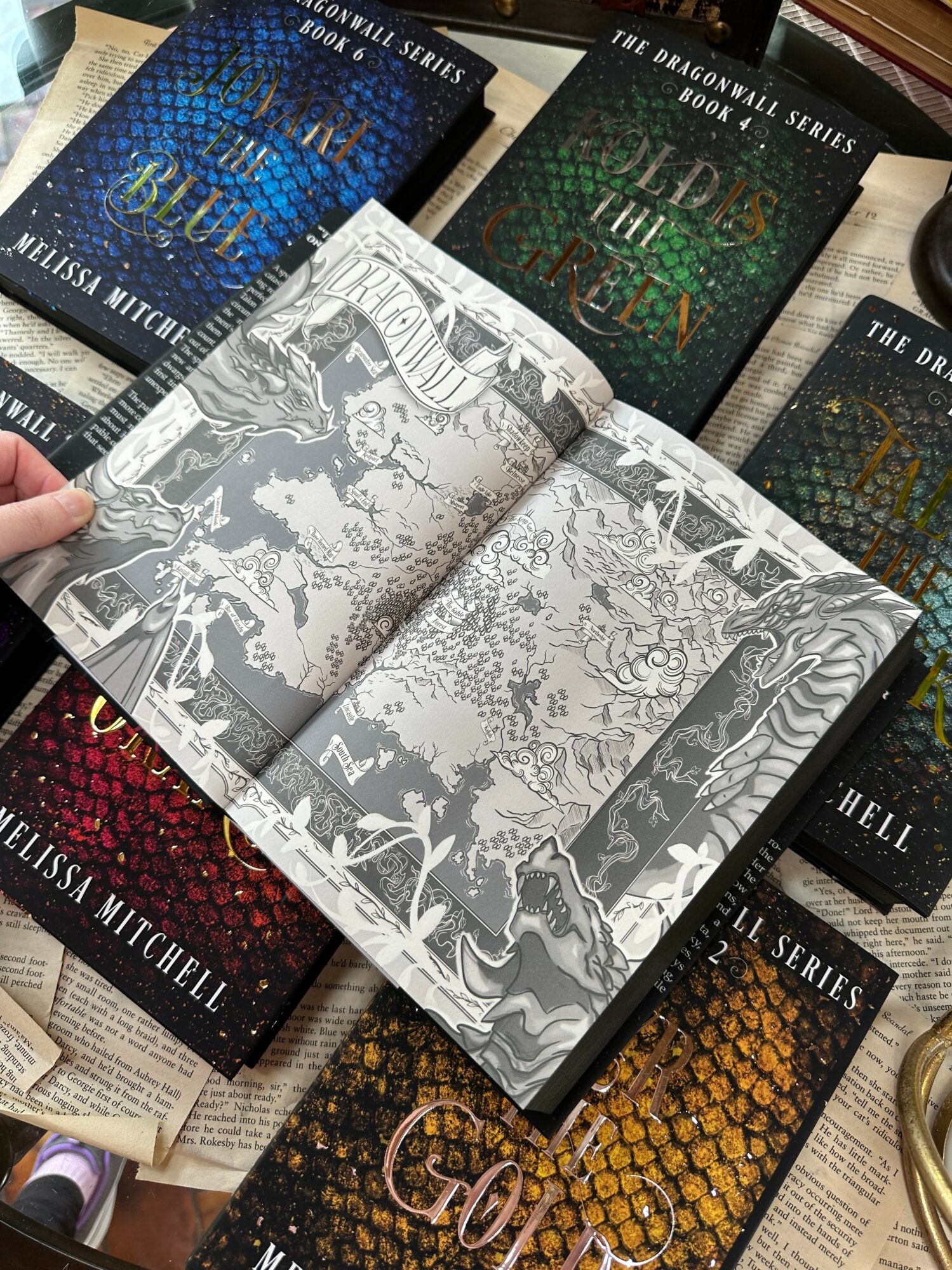 Open book with black and white illustrations on pages, surrounded by colorful books on a table.
