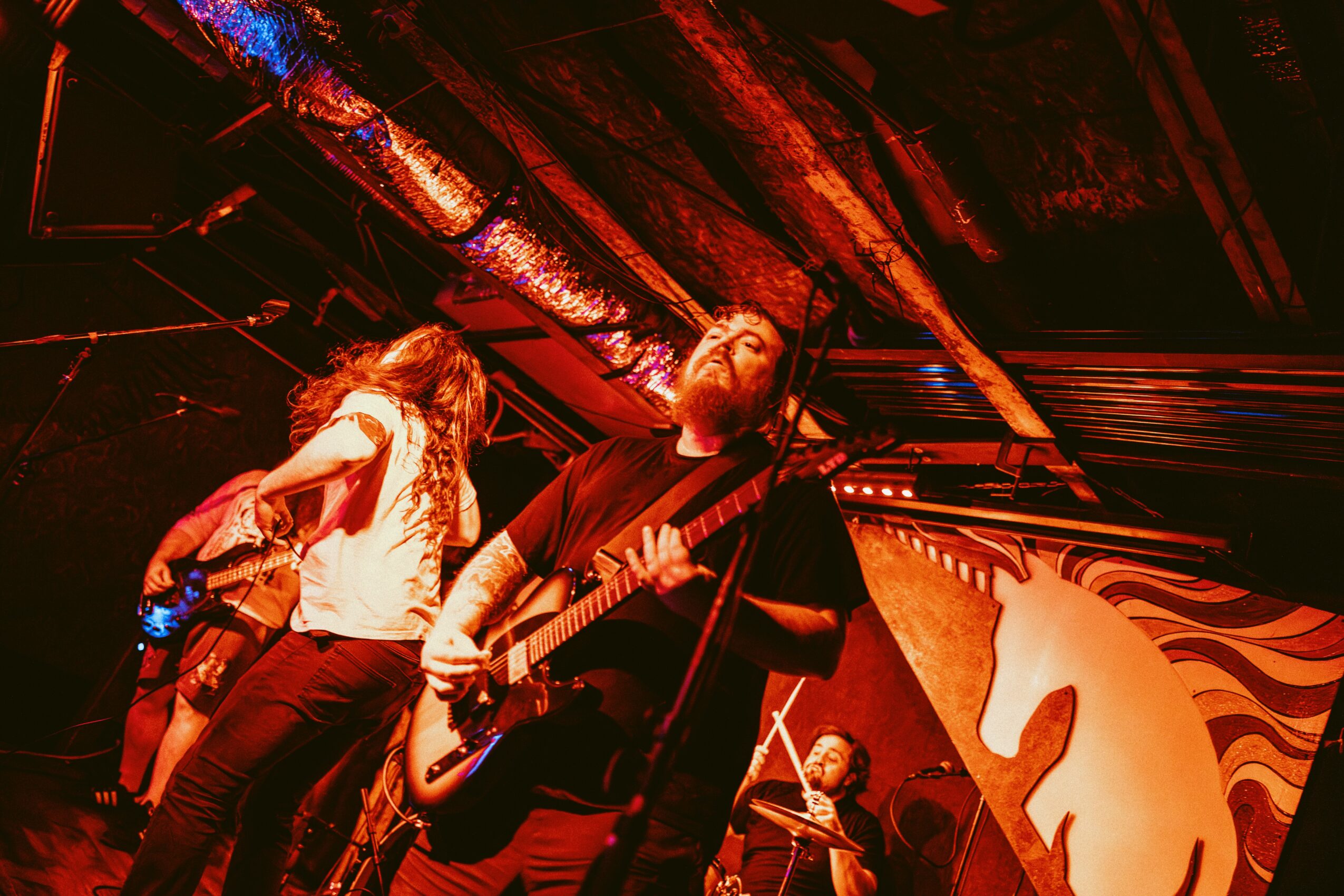 Musician playing guitar on stage with a colorful horse mural in the background, stage lighting creates a warm atmosphere.