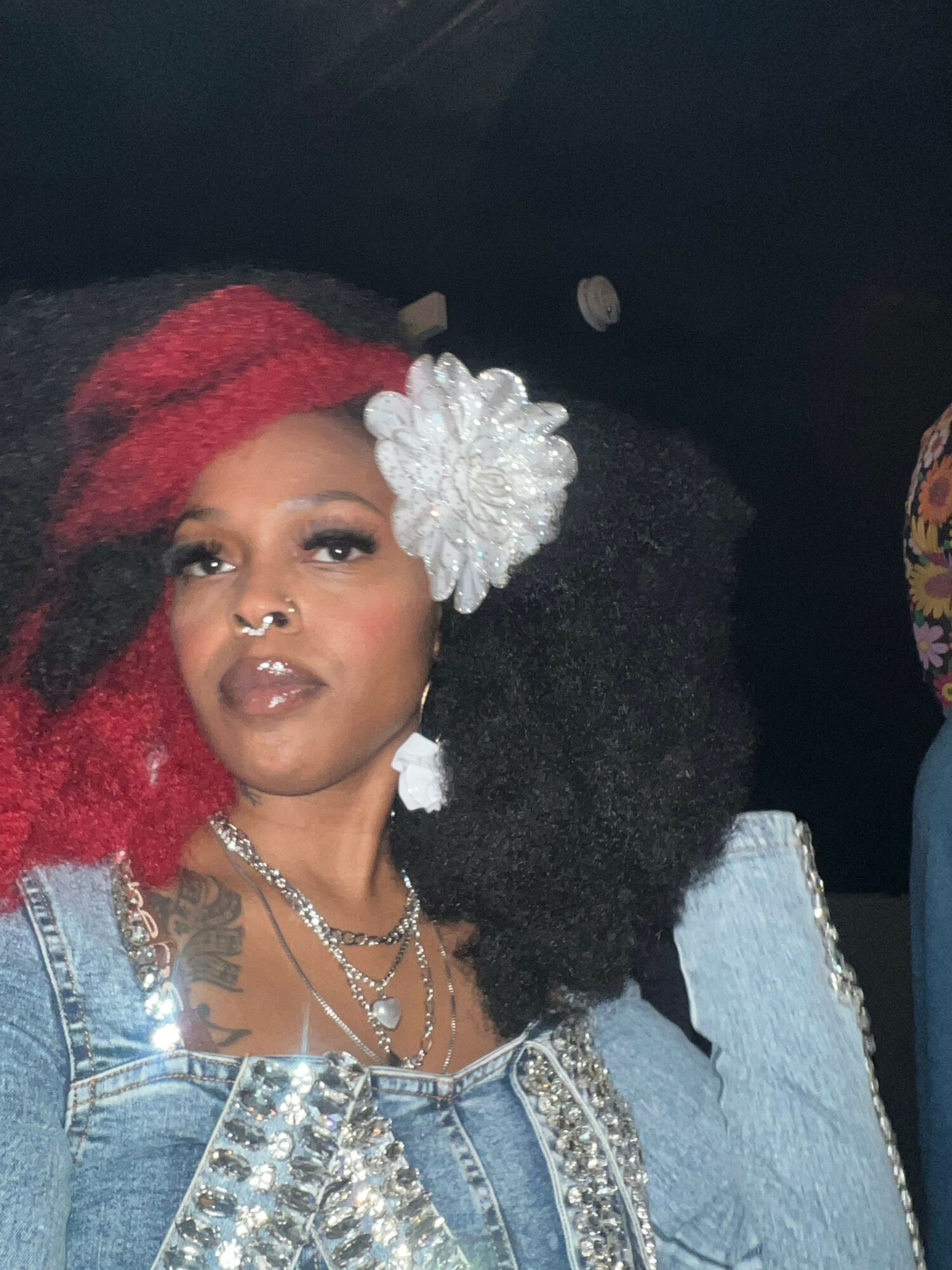 Woman with curly hair, wearing a red and white headband, denim jacket, and jewelry, lying down.