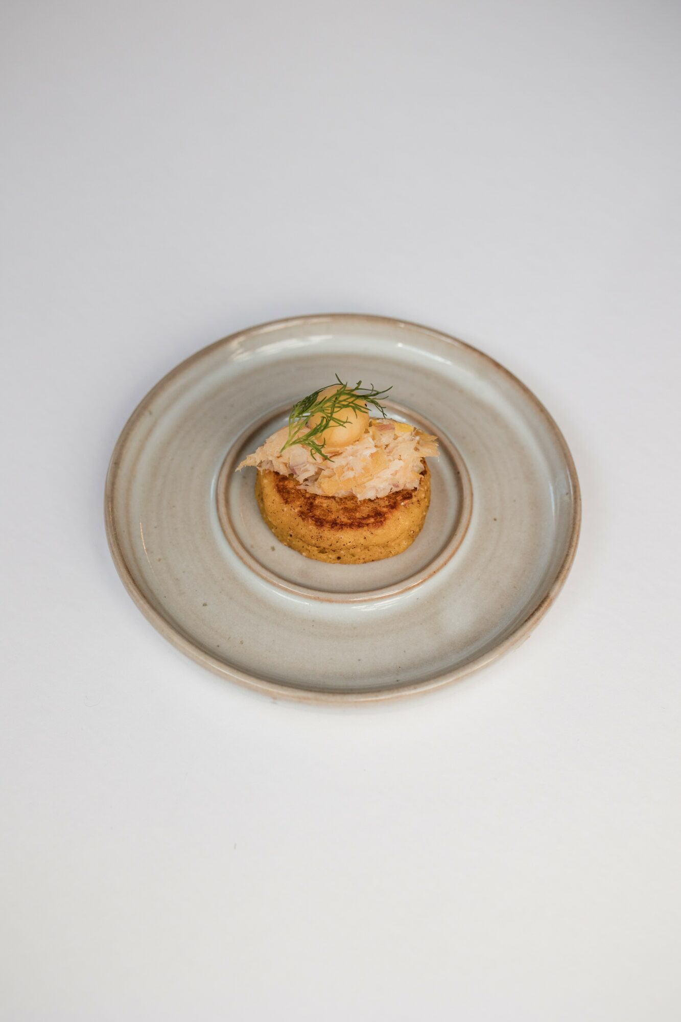 A small appetizer with a creamy topping and garnish on a round plate, viewed from above.
