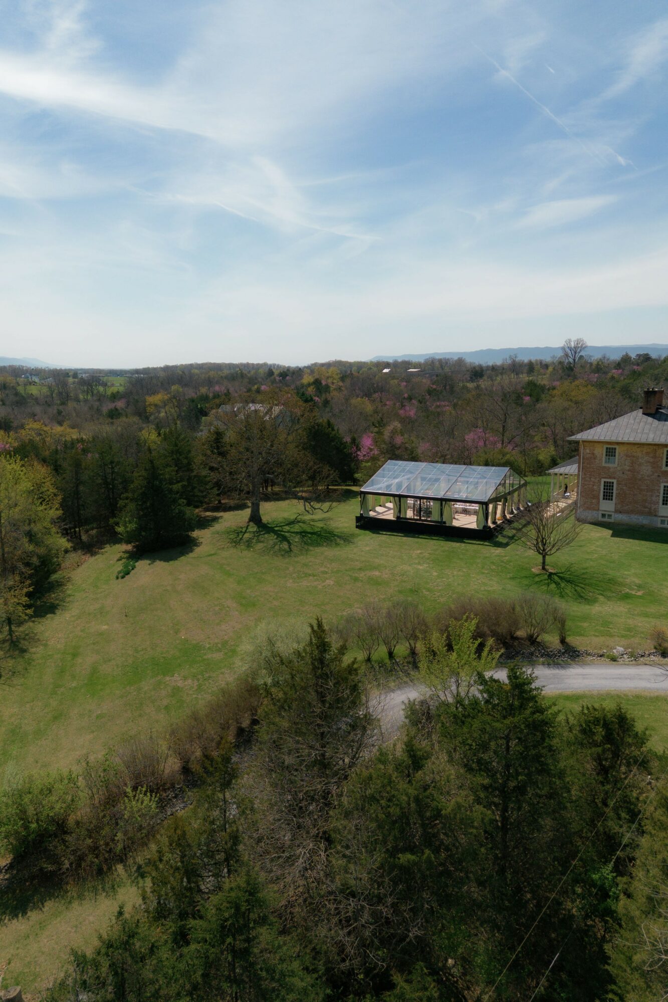 Landscape with trees, a building, and a house under a partly cloudy sky.