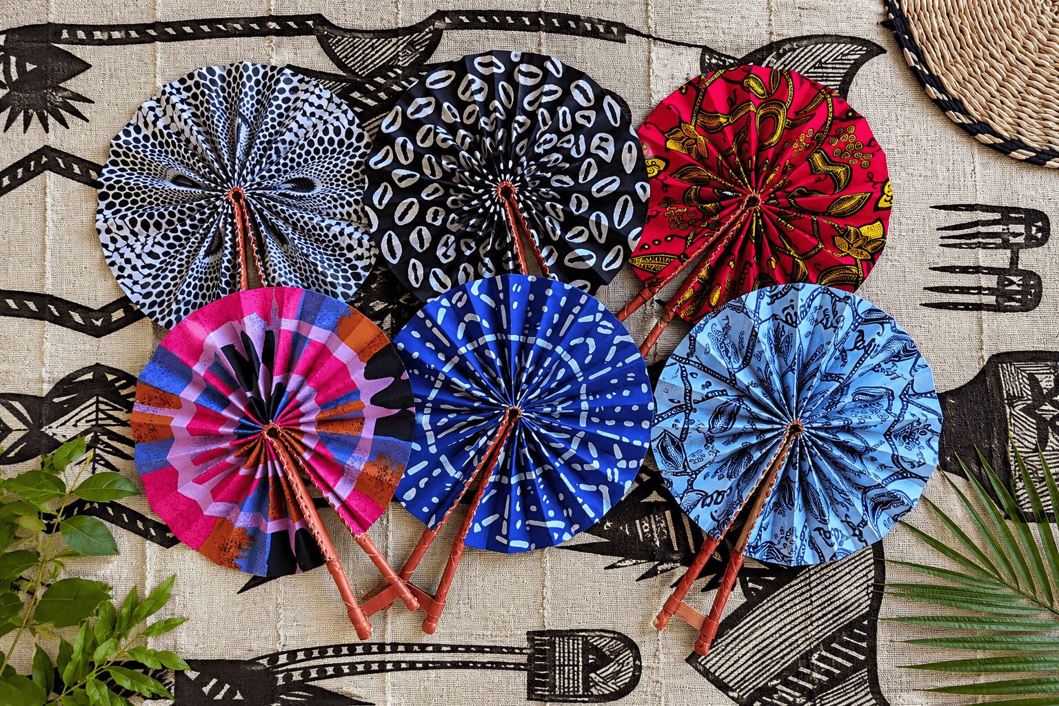 Six colorful paper umbrellas arranged on a fabric background with utensils and plant leaves nearby.