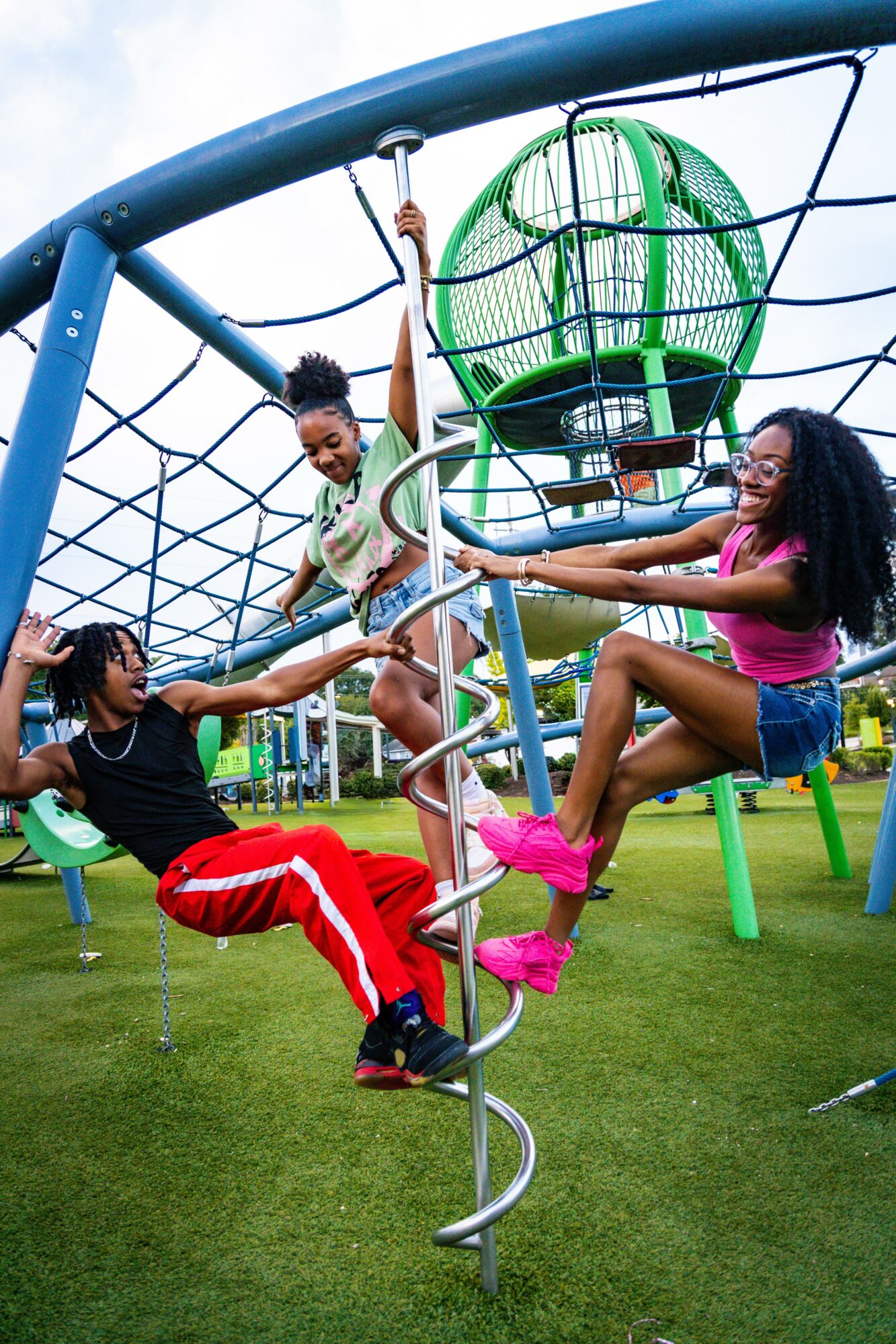 Four children playing on a playground climbing structure with a green spherical element, smiling and reaching out to each other.