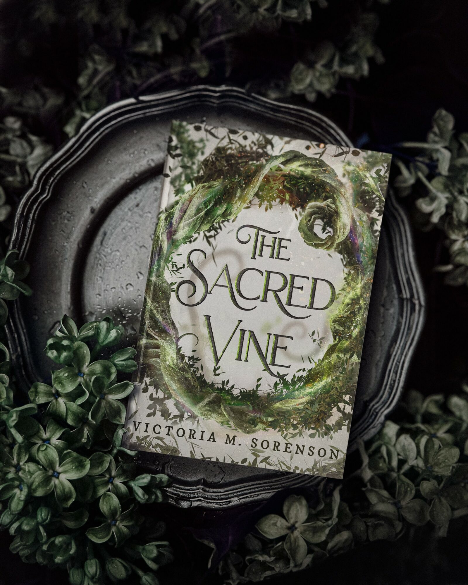 Book titled 'The Sacred Vine' by Victoria M. Sorenson on a decorative plate surrounded by greenery.