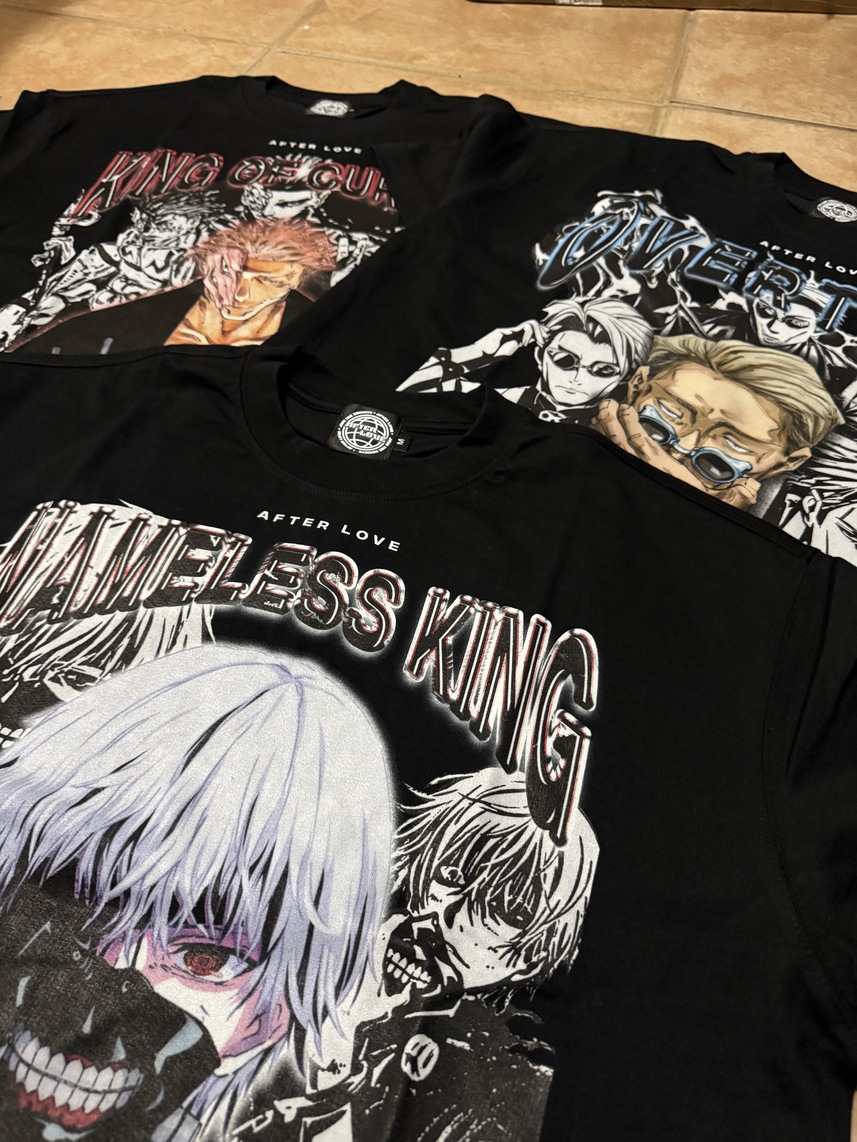 Four black T-shirts with colorful anime and manga-style illustrations laid on a wooden surface.