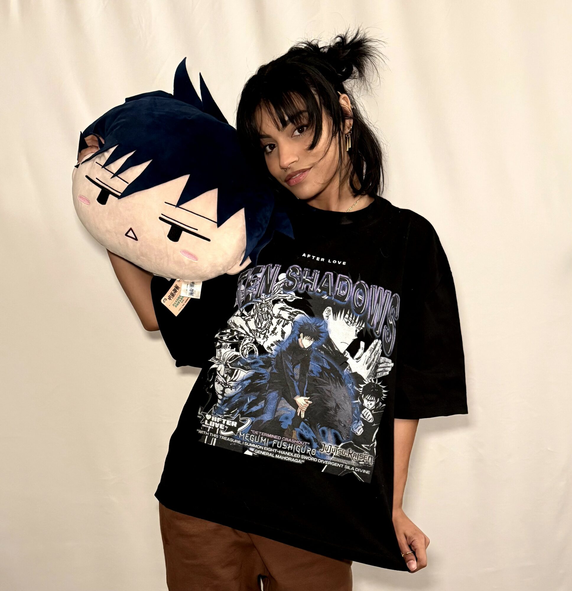 Person holding a large plush toy with spiky hair, wearing a black graphic T-shirt, standing against a plain background.