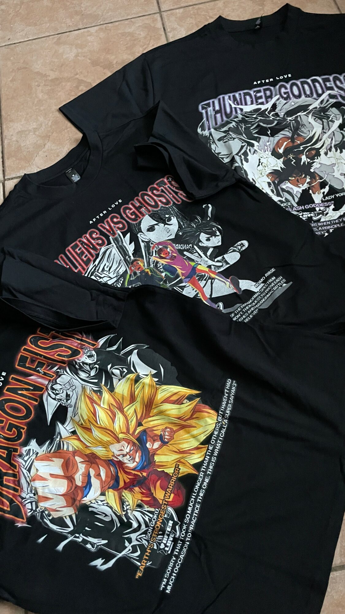 Three black T-shirts with colorful Dragon Ball Z and Thundercats graphic designs laid flat on a surface.