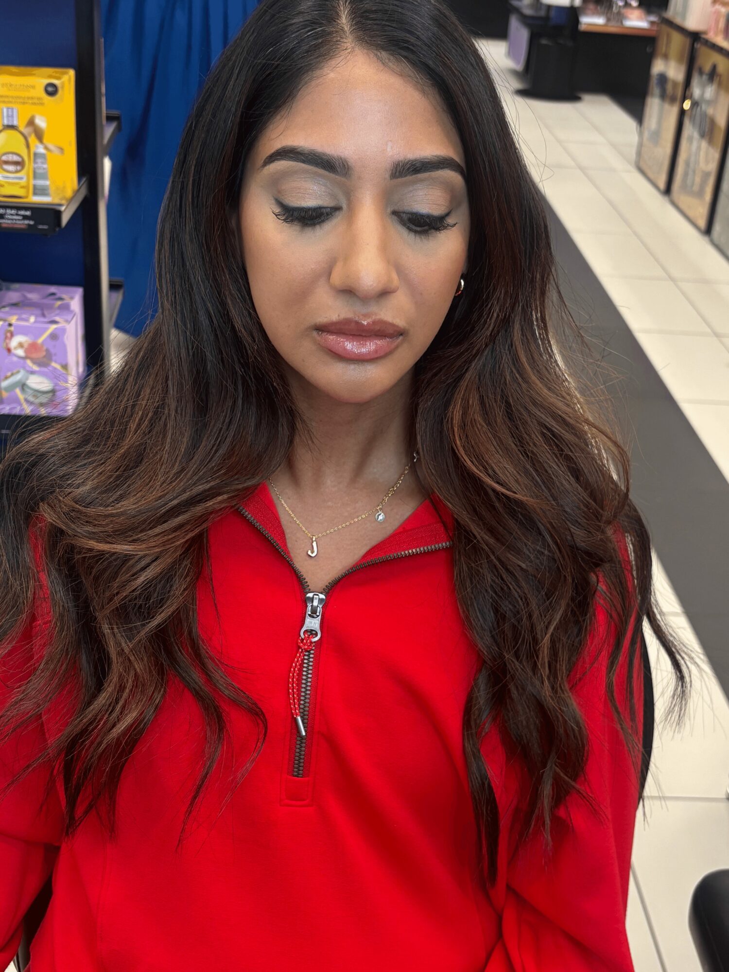 Woman with long wavy hair wearing a red zip-up top in a store aisle.