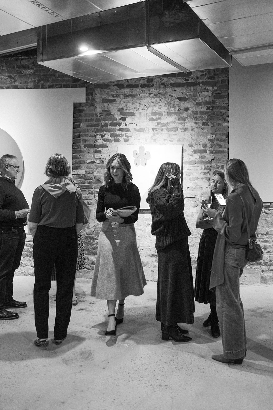 Group of people standing and talking in an art gallery with brick wall background.