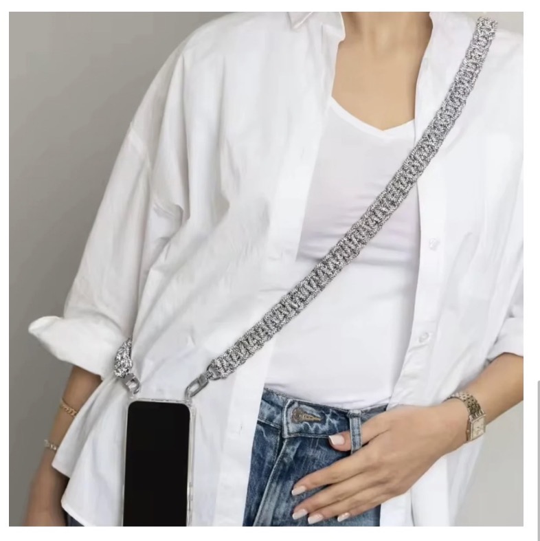Person wearing a white shirt, white t-shirt, jeans, with a phone in a strap across the chest, and a watch on the wrist.