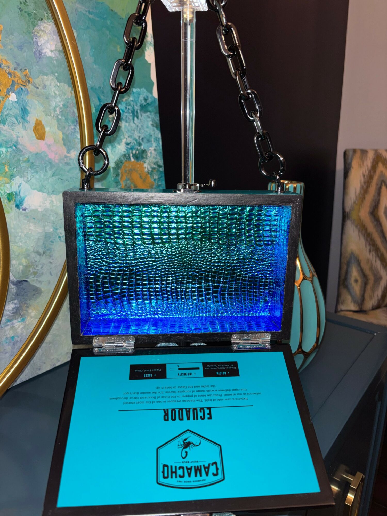 Laptop with a blue screen displaying a logo and text, connected to a chain, on a desk.