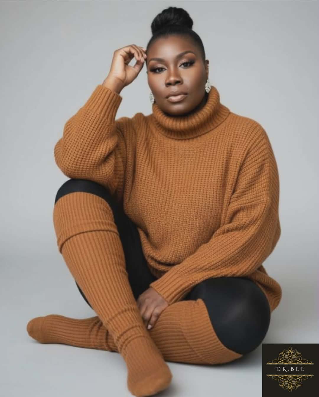 Woman sitting cross-legged in a brown sweater and matching socks, with a neutral background.