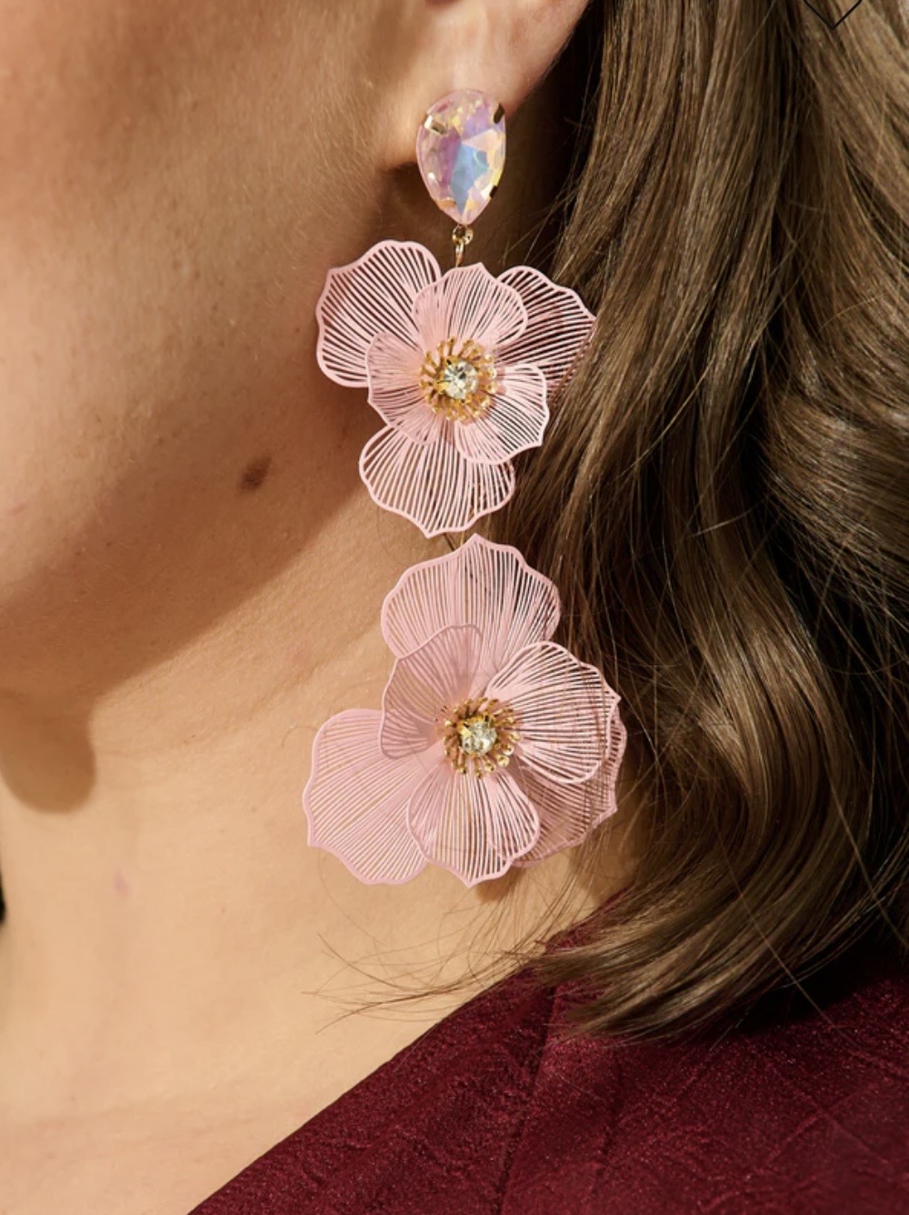 Close-up of a woman's ear with a large pink floral earring featuring three flowers with gold centers.