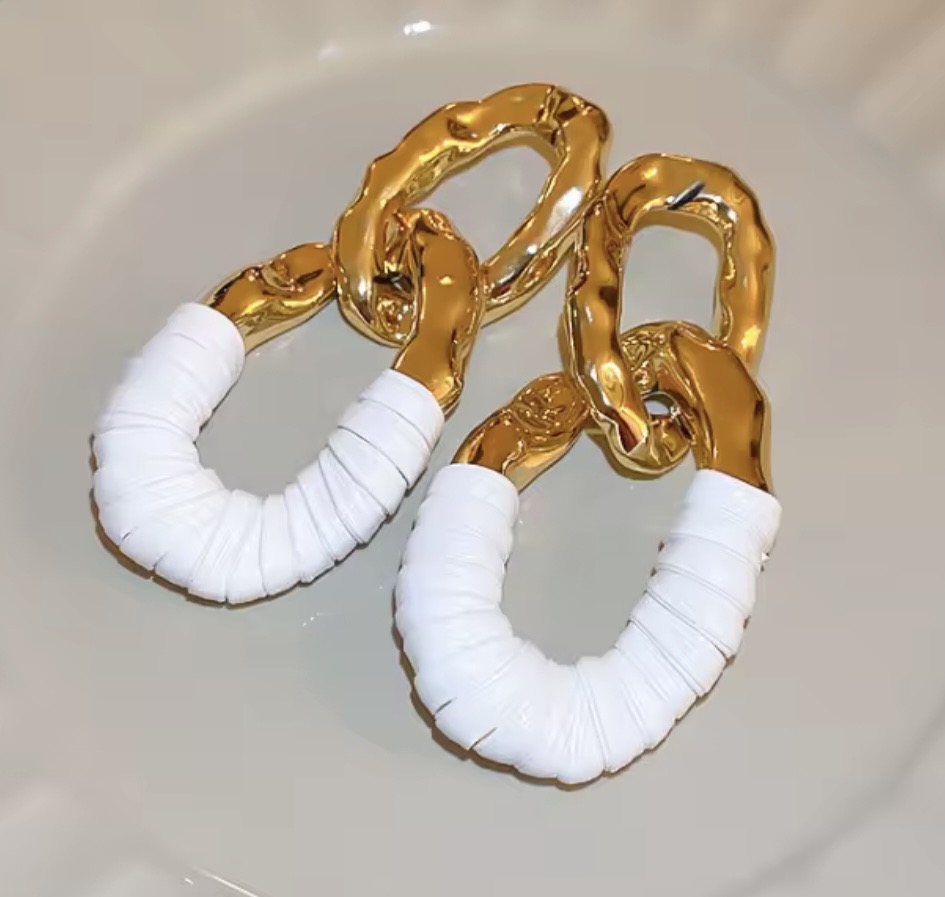 Gold chain earrings with white wrapped hoops, on a light background.