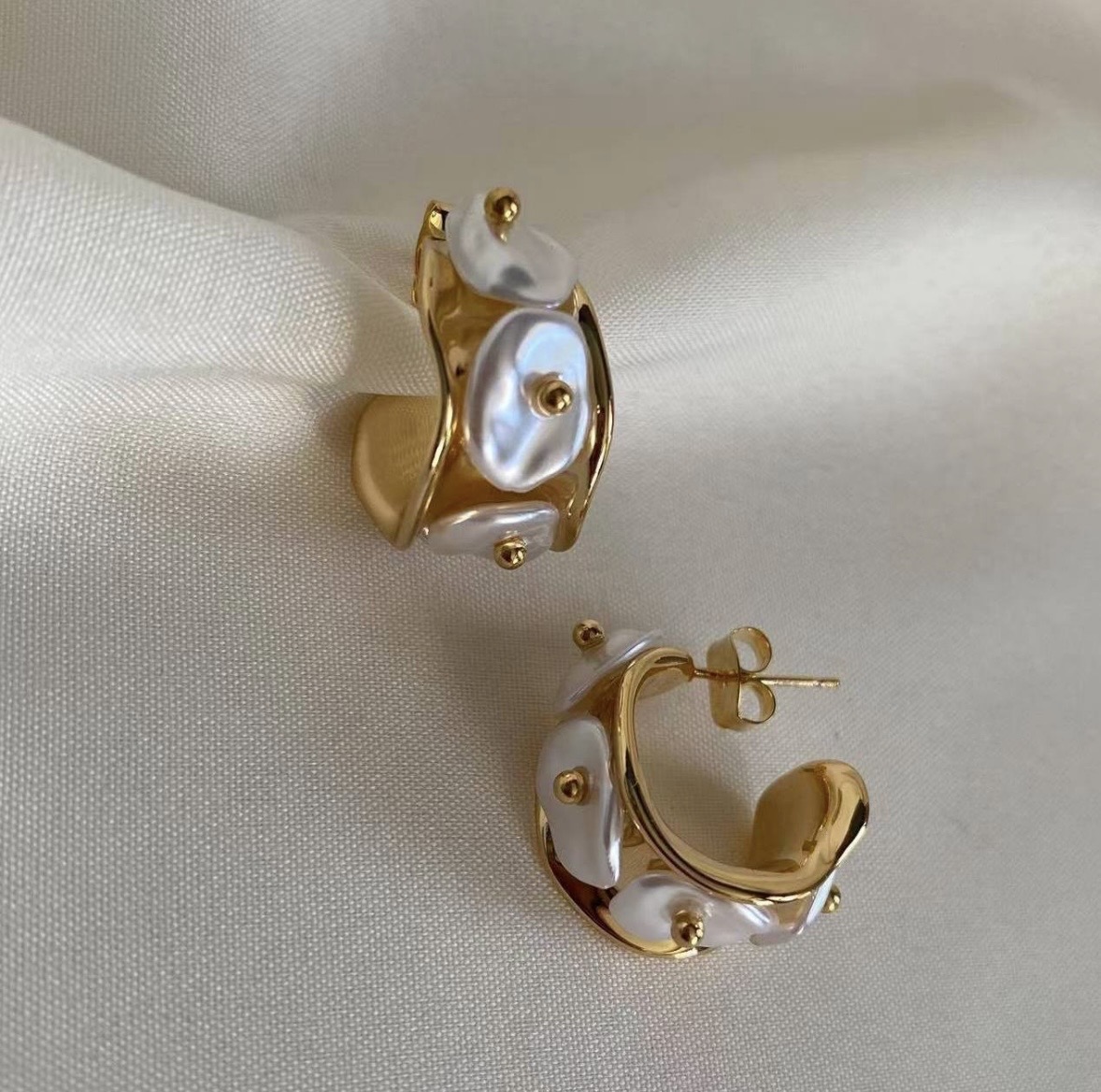 Gold hoop earrings with white pearls on a white fabric background.