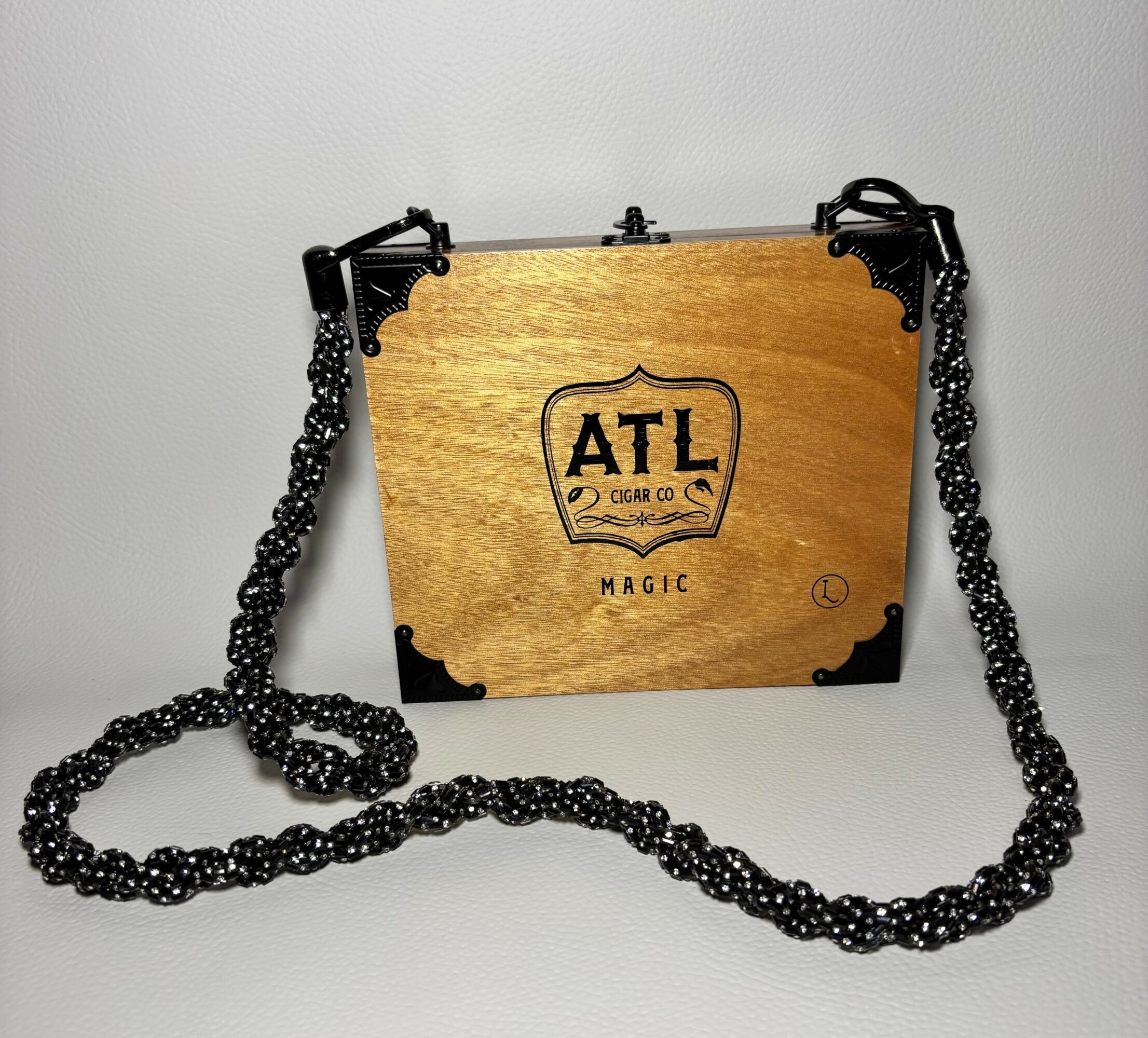 Wooden box with black chains on sides, engraved with ATL logo and text, against a plain background.