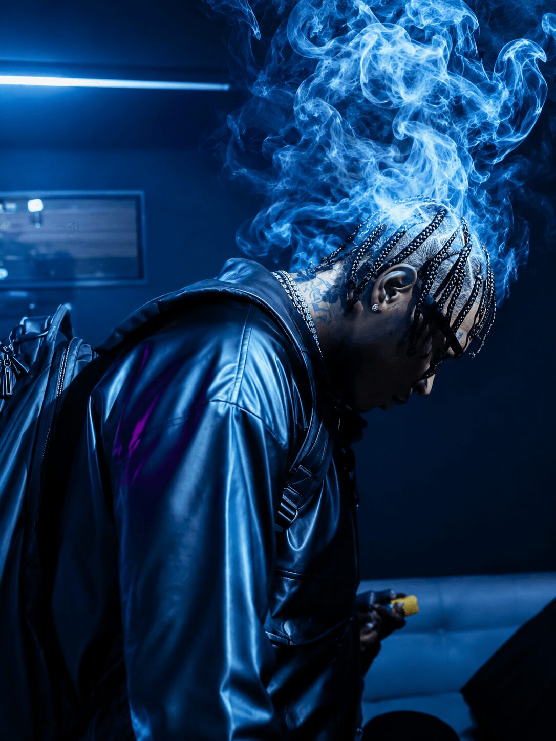 Person with braided hair in a shiny jacket, smoke around head, dark background, blue lighting.