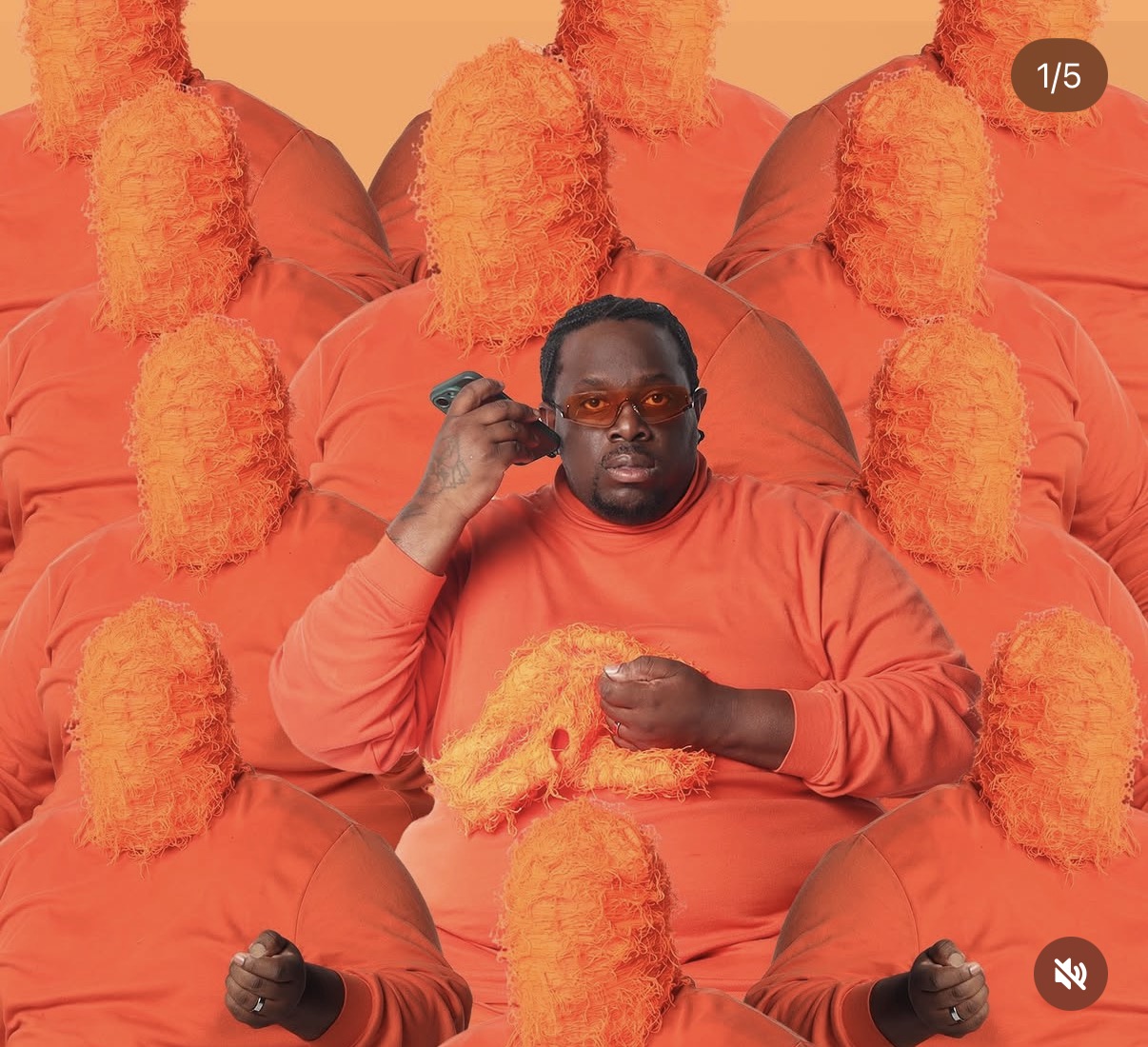 Person with glasses and beard in orange clothing surrounded by orange fluffy objects, holding a fluffy object, against an orange background.