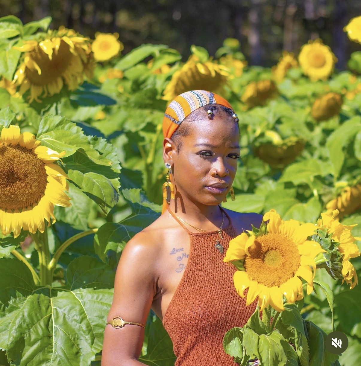 Woman with headscarf and earrings among sunflowers in a sunny field.