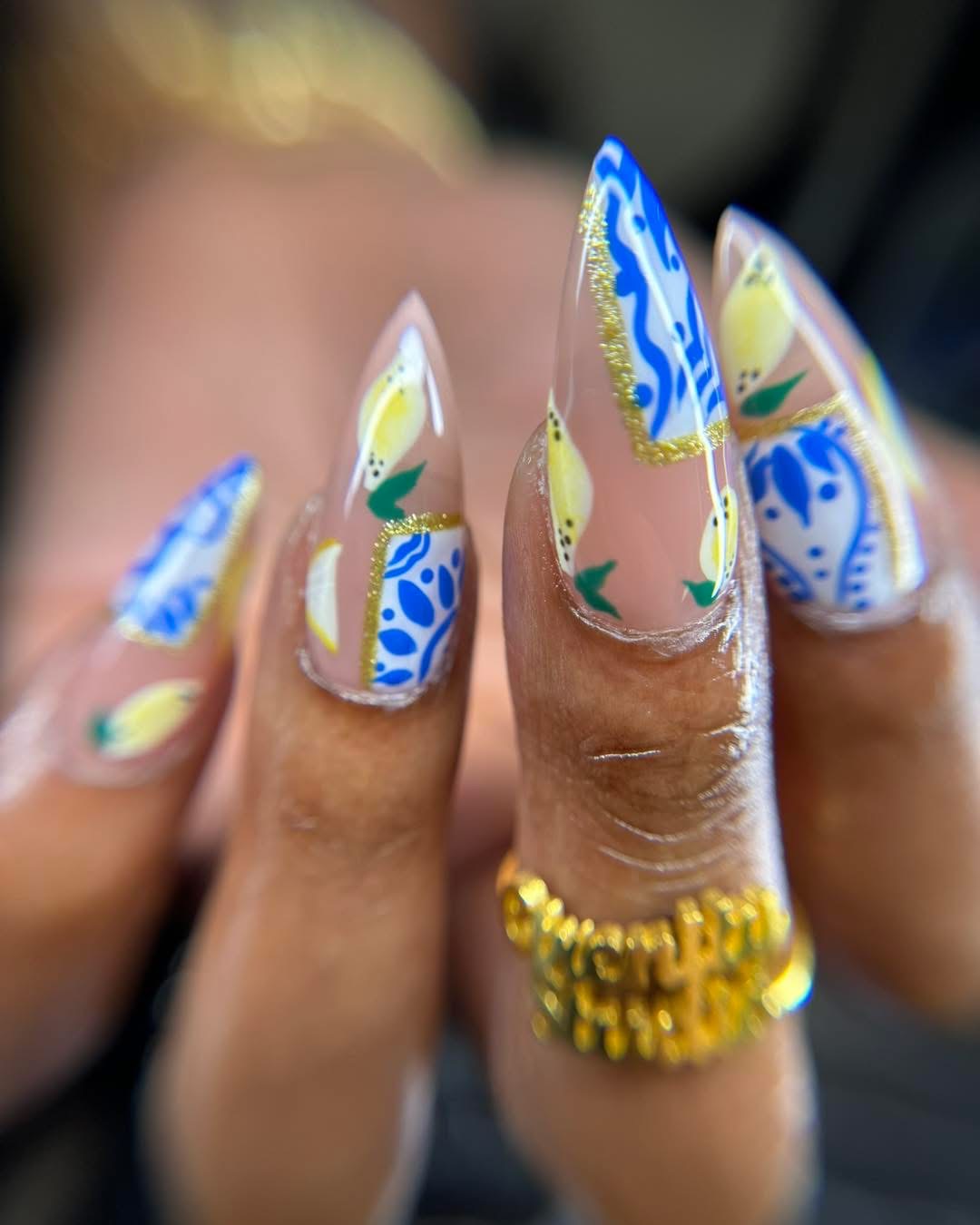 Close-up of decorated fingernails with blue, yellow, and white patterns, and a gold ring on the middle finger.