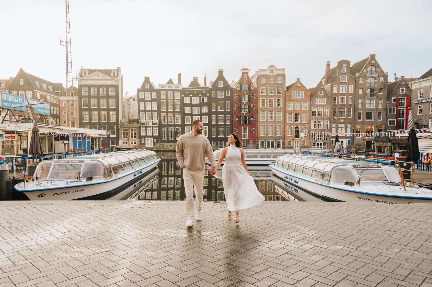 Couple walking along a harbor with boats and colorful buildings in the background.