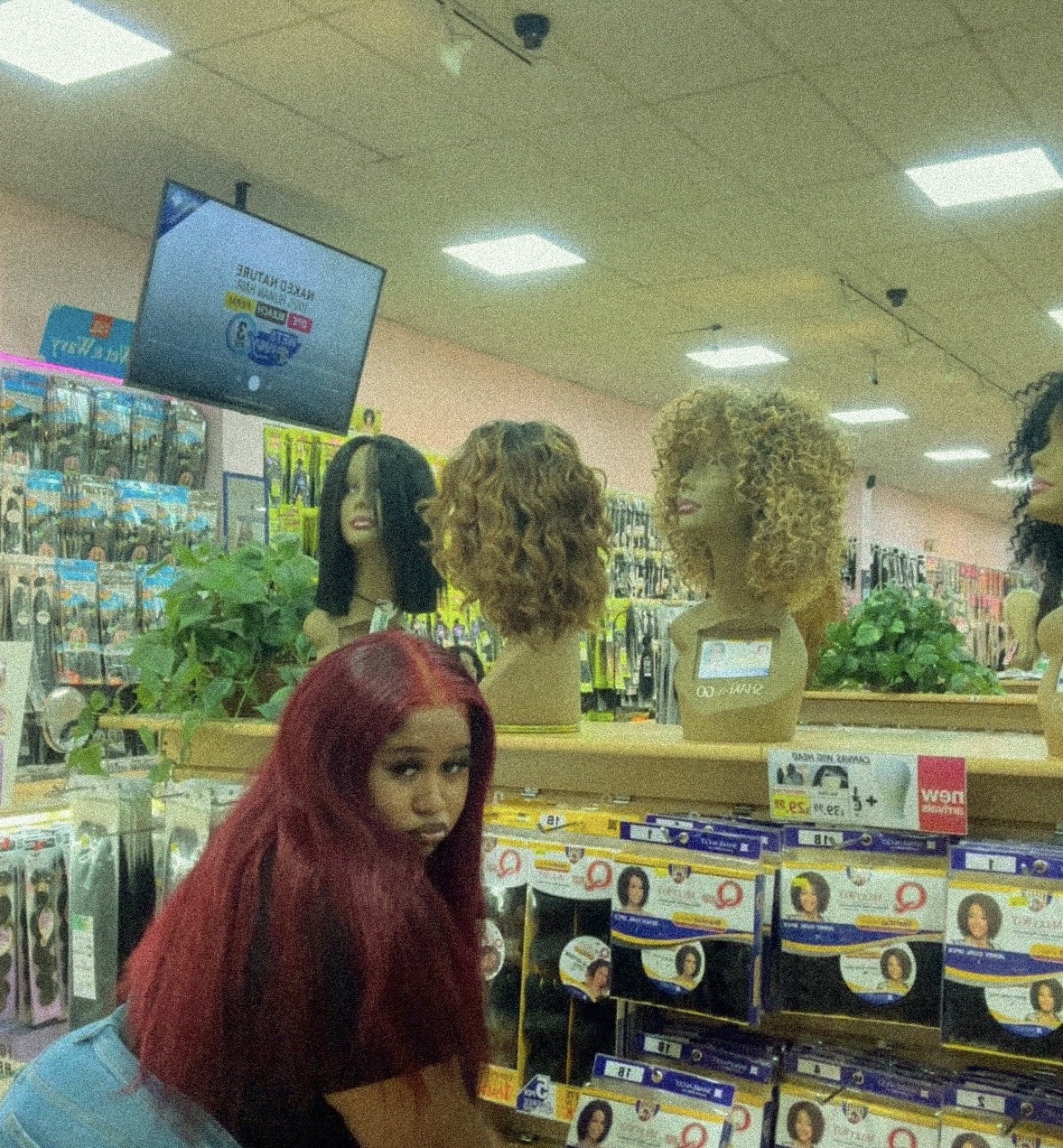 Store display with mannequin heads and a person with long red hair in the foreground.