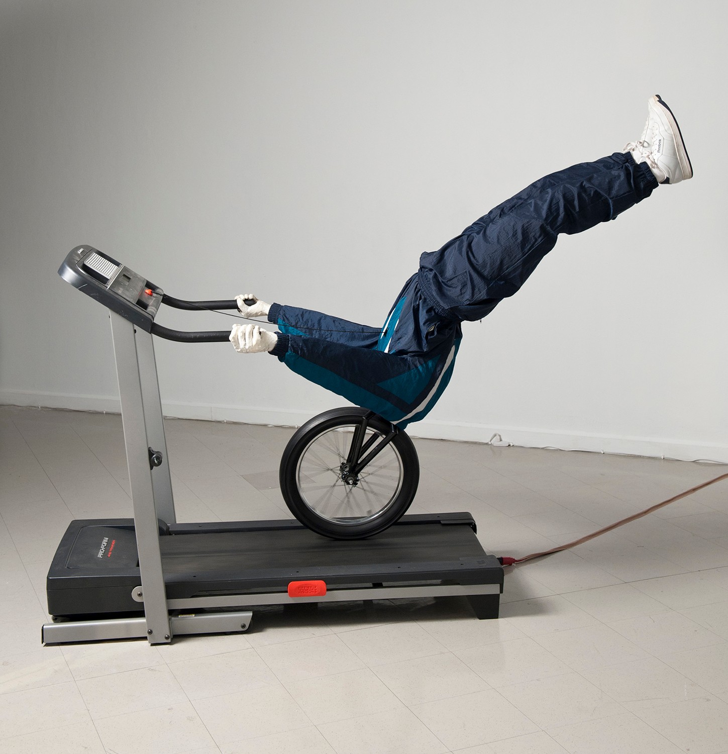 Person with legs raised on treadmill, holding handles, in a room with plain white wall, wearing dark pants and white shoes.