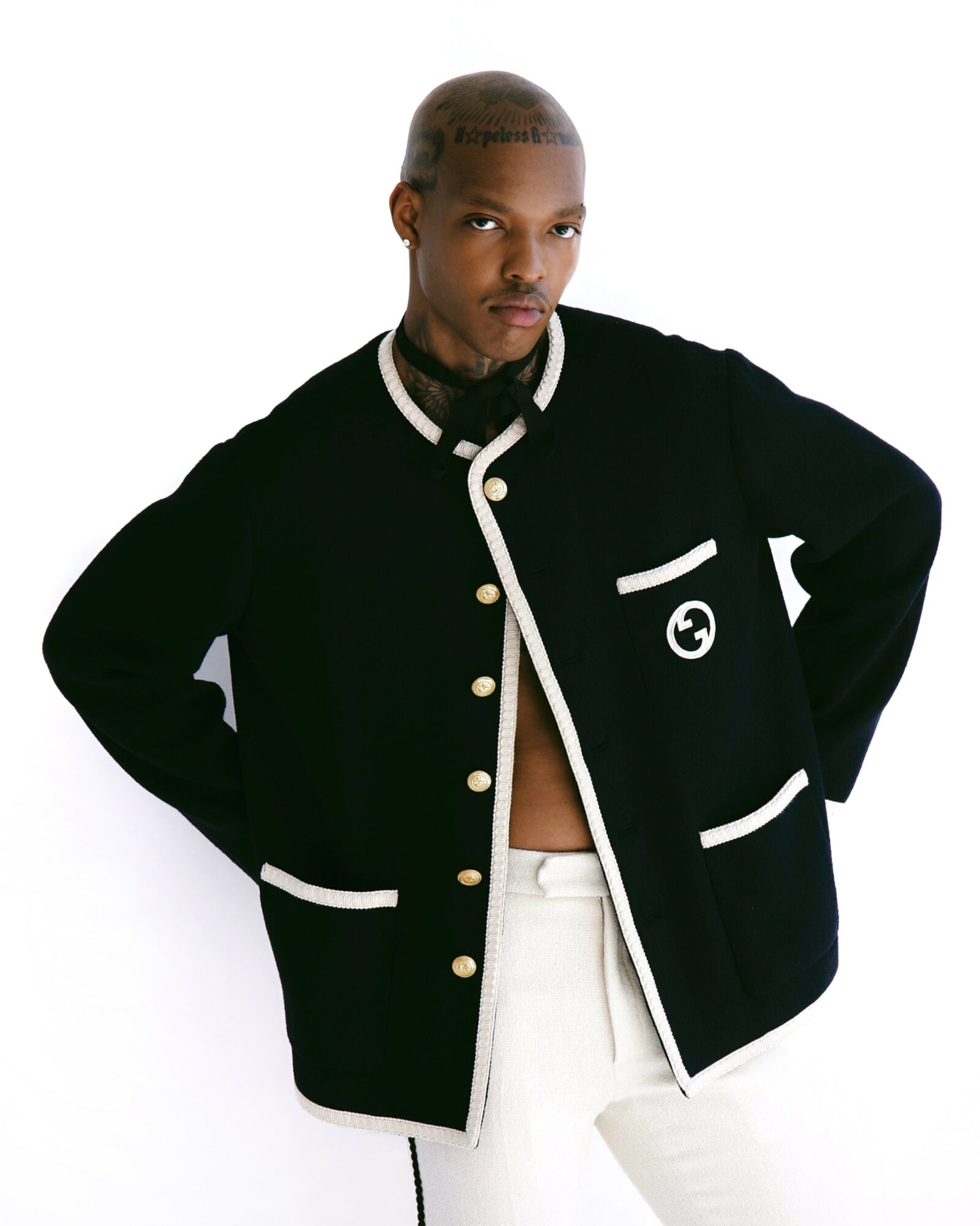 Person with short hair wearing a black jacket with white trim, standing with hands on hips, against a white background.