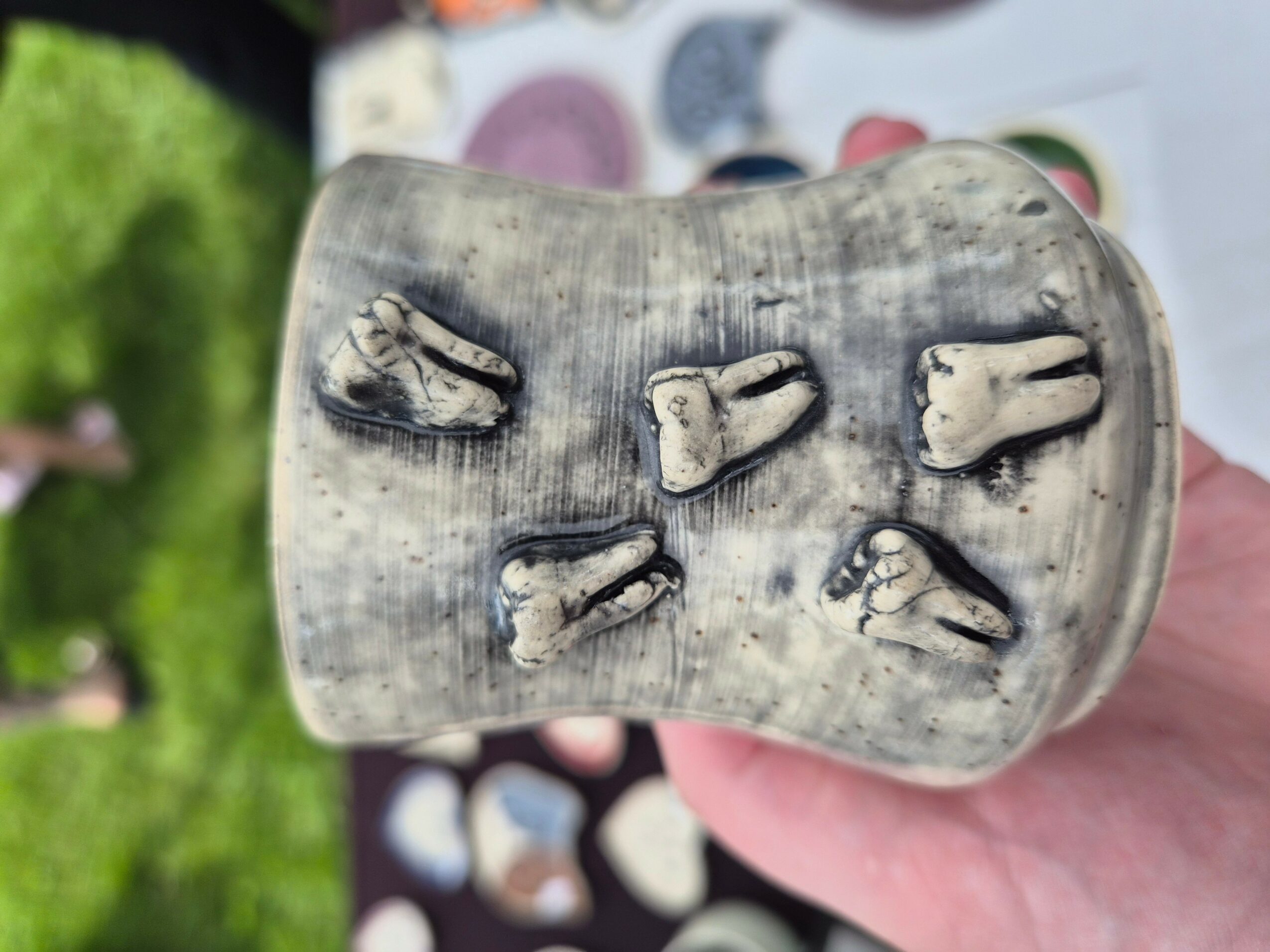 Close-up of a weathered, grayish bone with multiple smaller bones embedded in it, held by a person's hand outdoors.