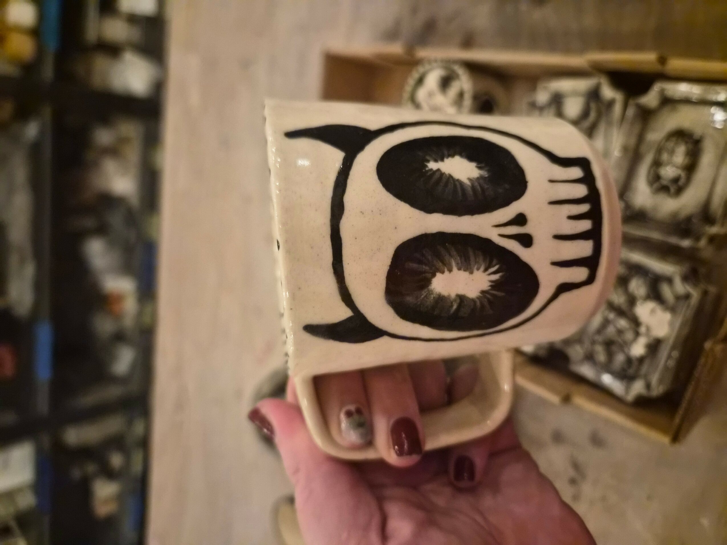 Person holding a cloth with a black and white owl face design, background shows shelves with decorative items.