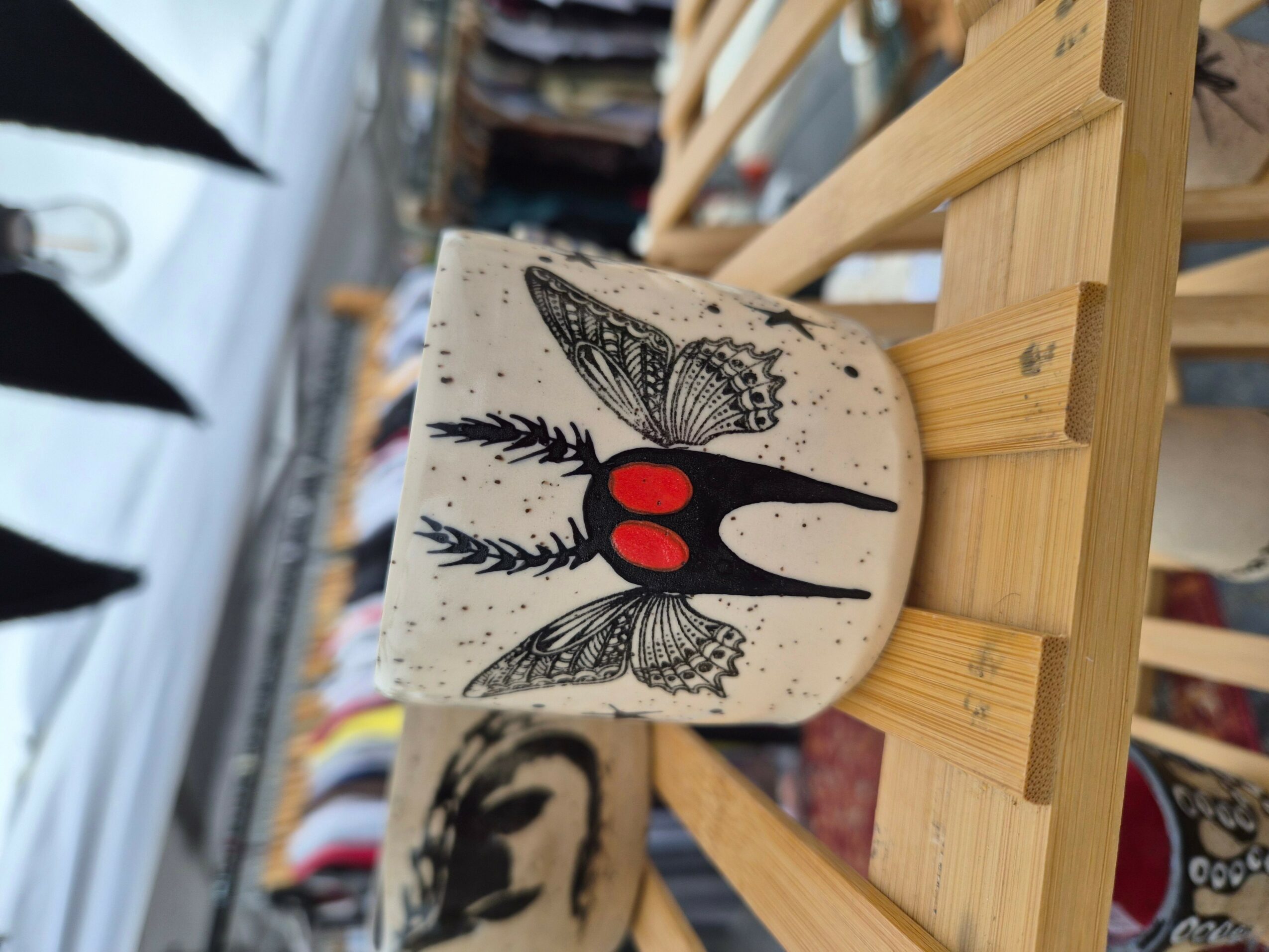 Decorative wooden object with a black and red design, placed on a wooden rack in a store.