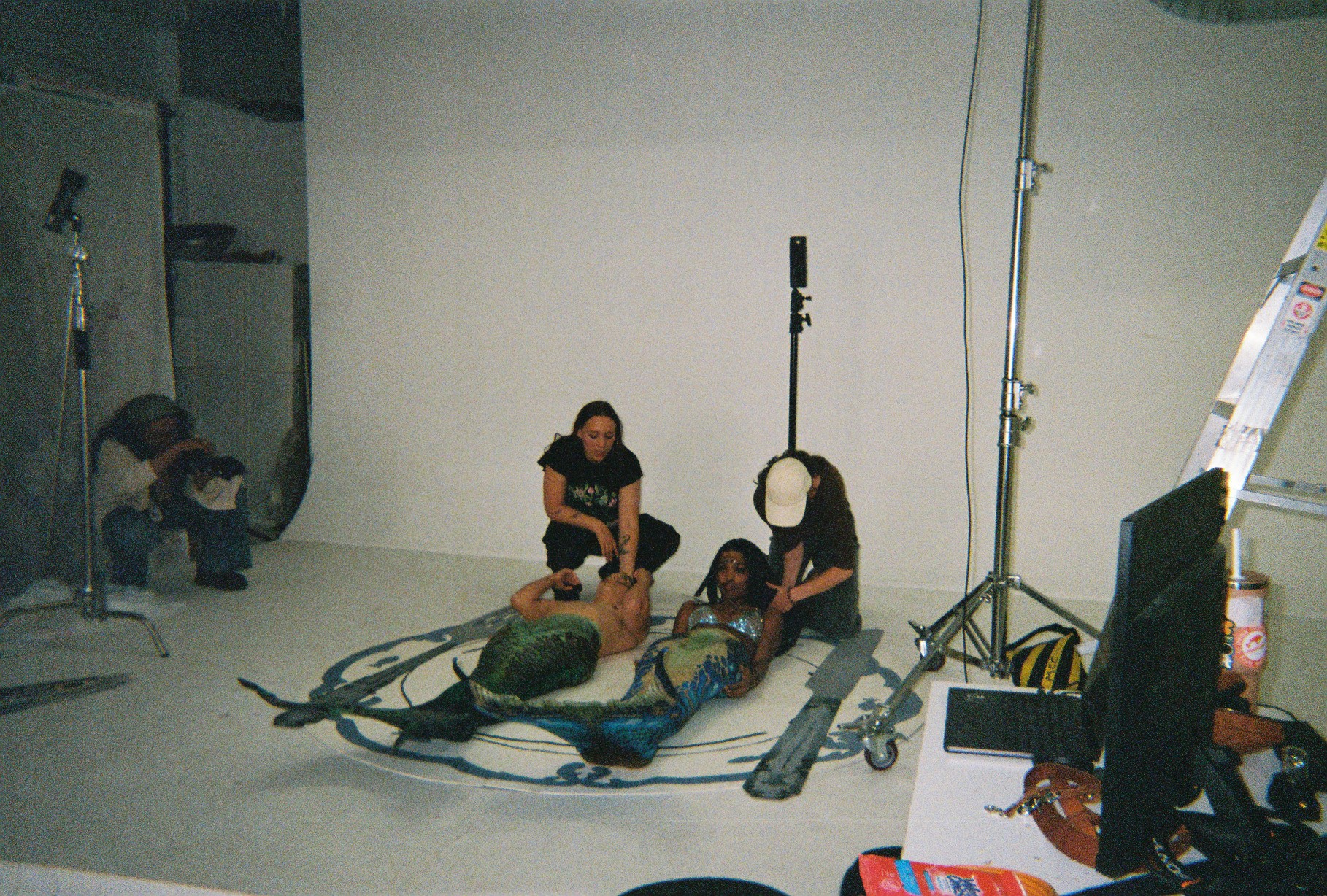 Two people sit on the floor with a large, colorful object, while a person in the background takes photos in a studio.