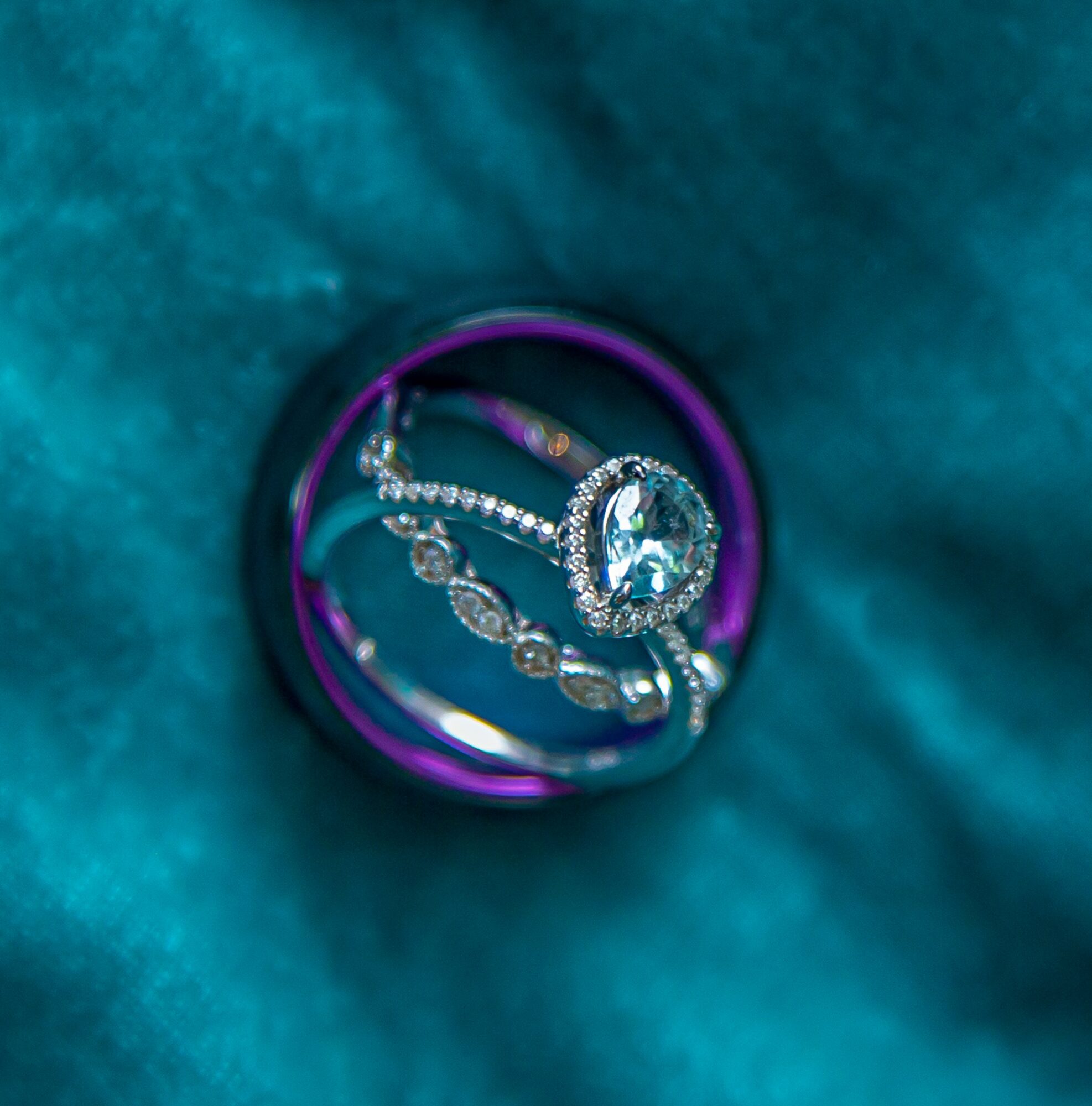 Close-up of a ring with a large central gemstone surrounded by smaller stones, placed inside a purple ring, on teal fabric.