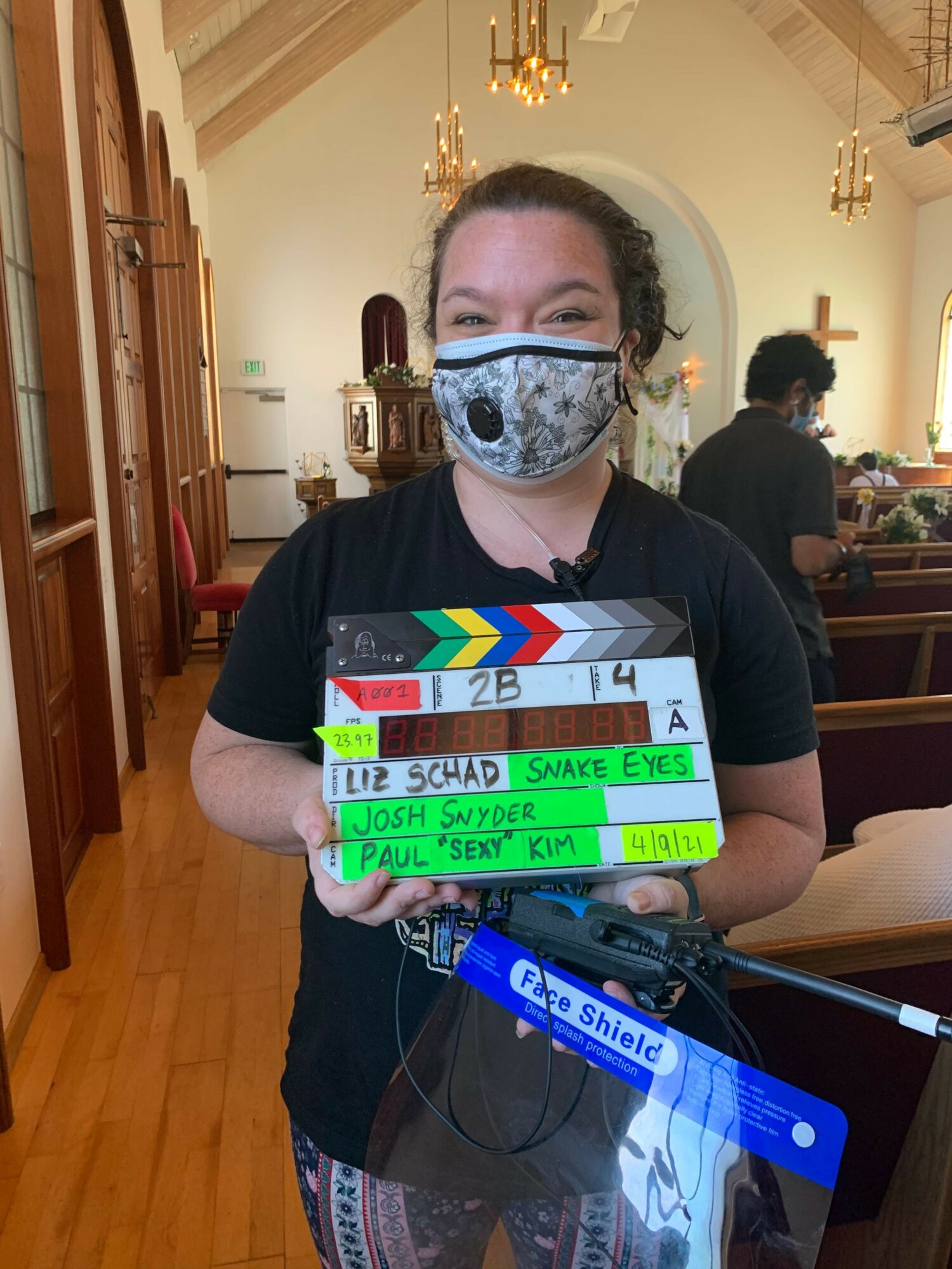 Person wearing a face mask holding a film slate in a room with wooden floors and furniture.