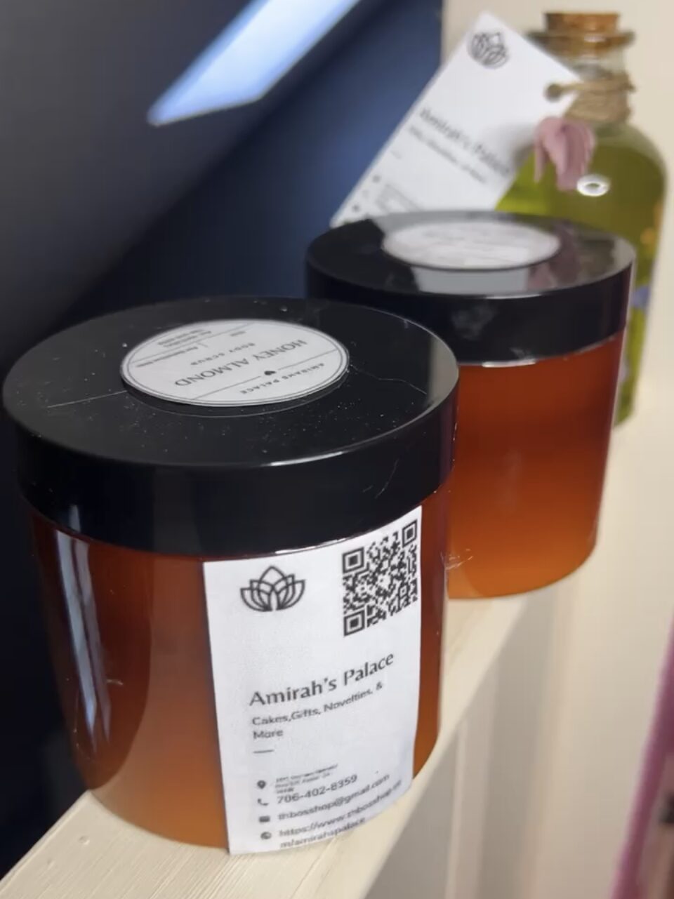 Two amber-colored jars with black lids on a surface, with a white label and QR code on one jar, and a blurred background.