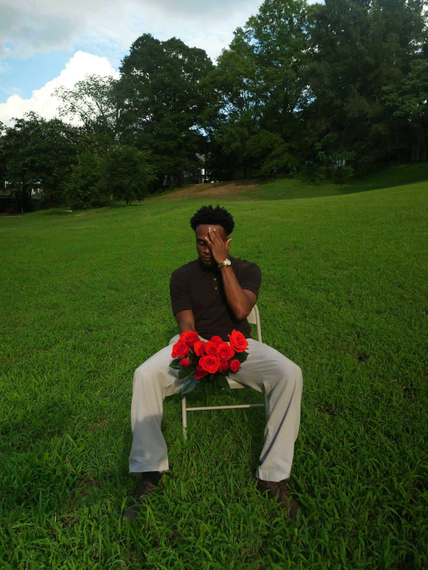 Person sitting on grass holding a bouquet of red flowers, with trees and sky in the background.