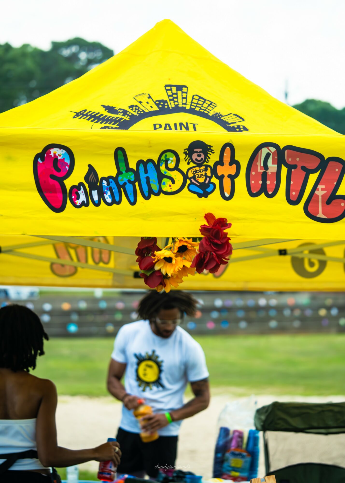Children playing under a yellow tent with colorful text and flowers, outdoors on a grassy field.