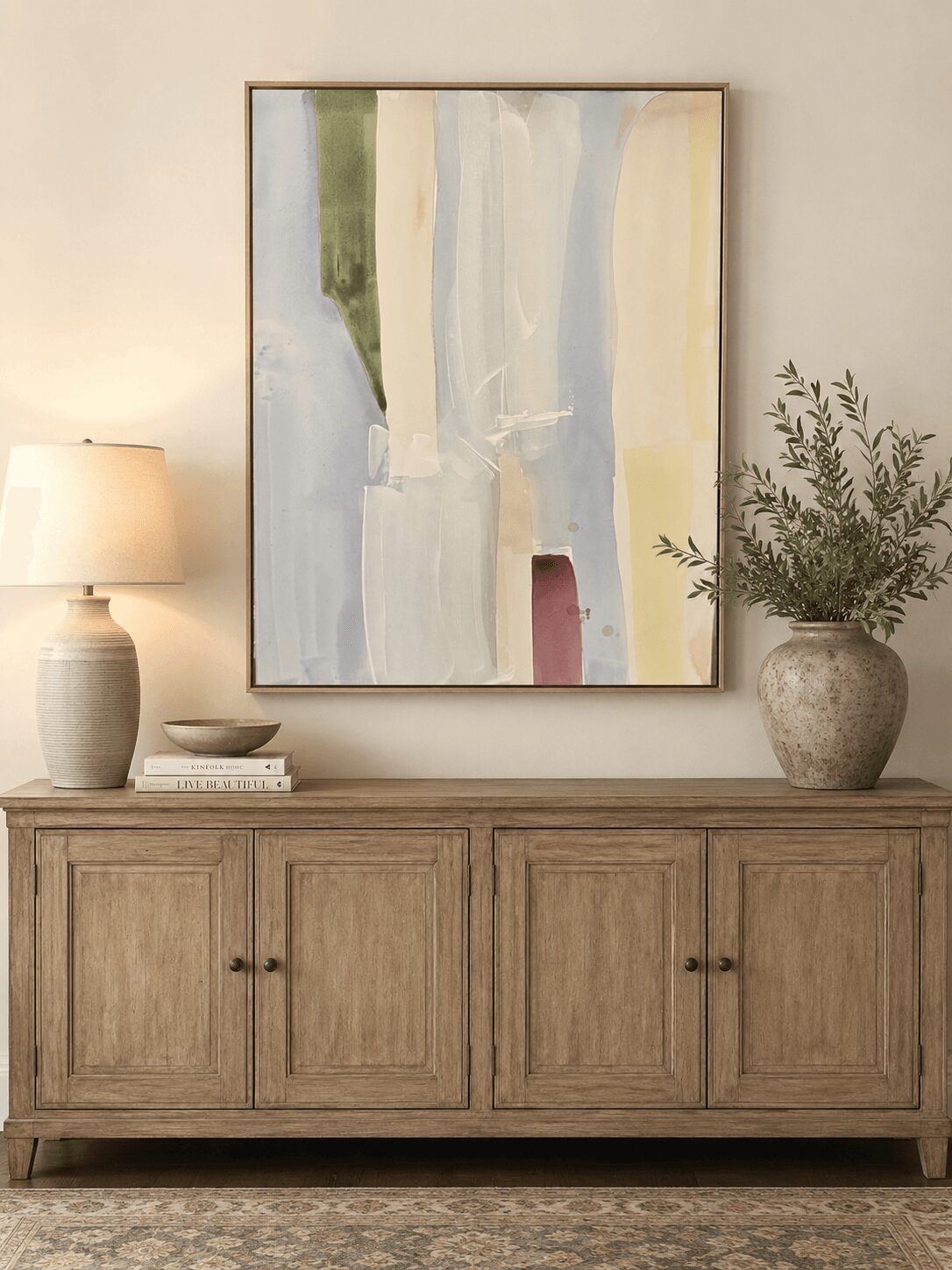 Abstract painting with vertical streaks in green, white, blue, and red hangs above a wooden sideboard, with a lamp and potted plant.