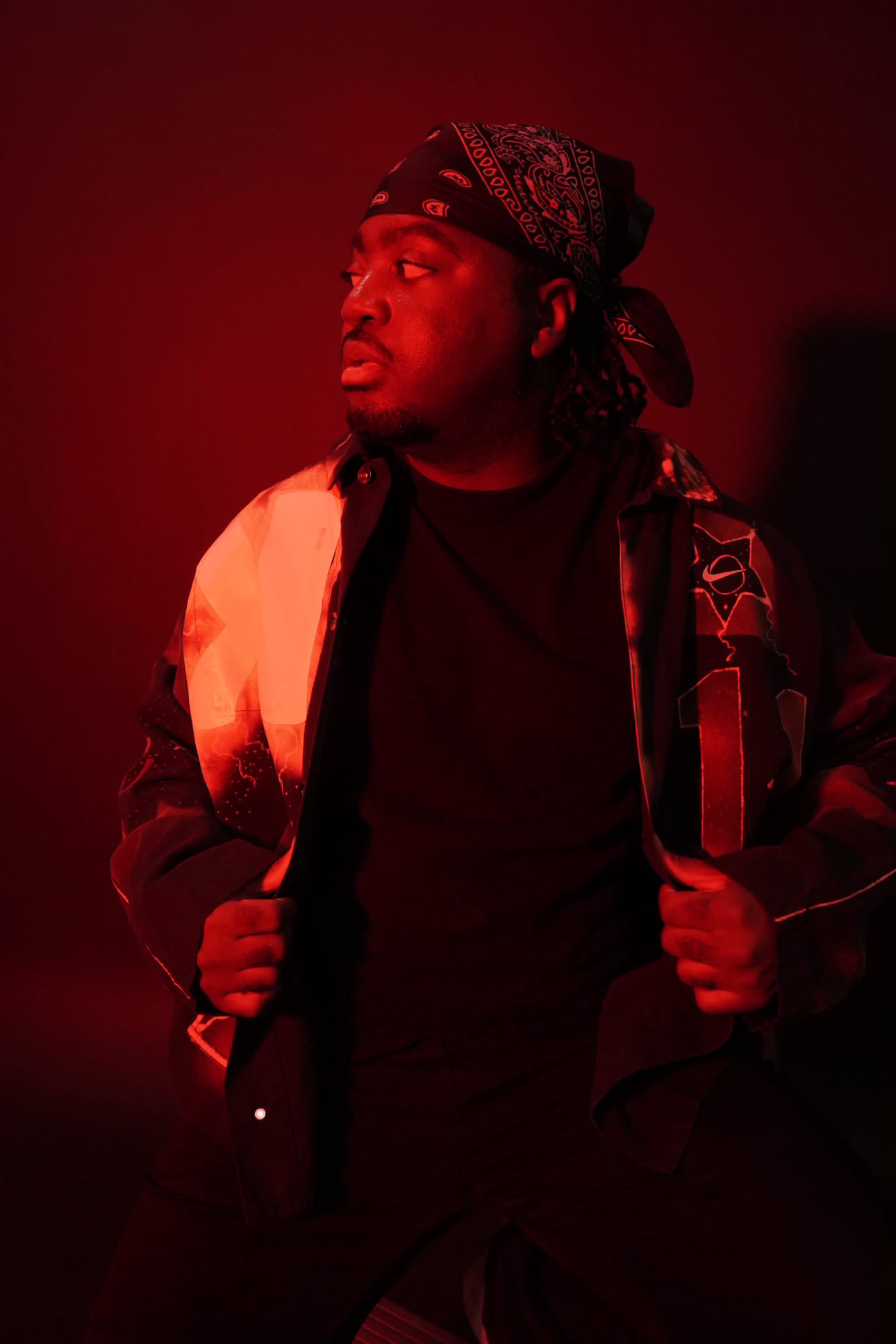 Person with a bandana and backpack, looking to the side, illuminated by red lighting.