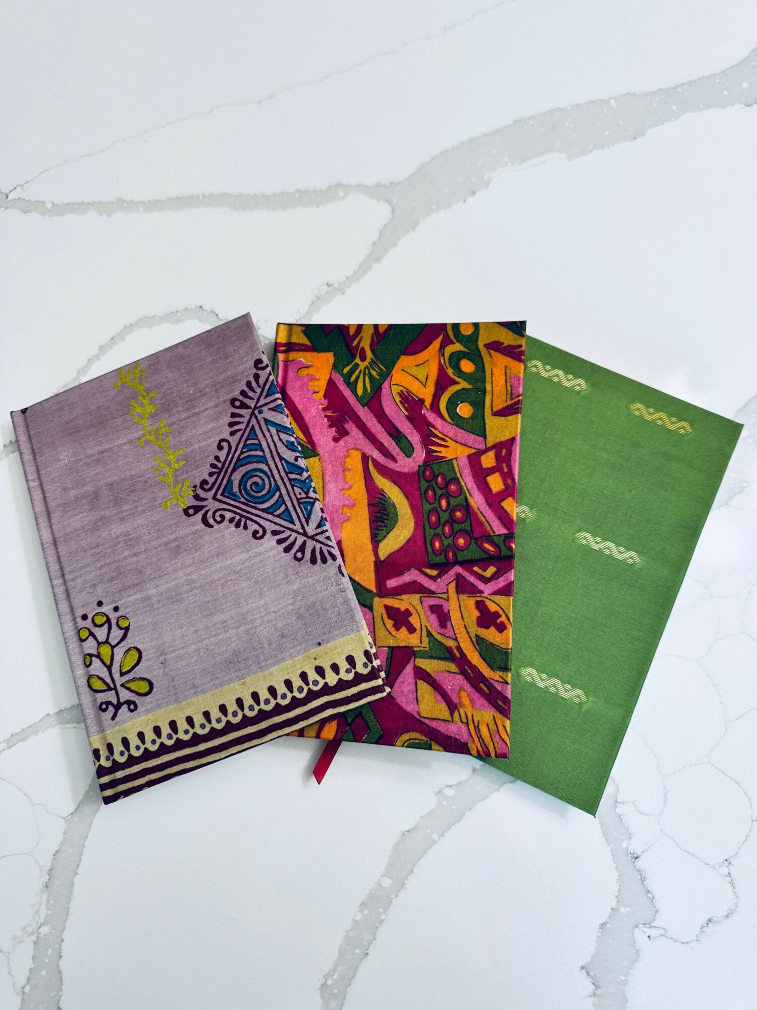 Three colorful notebooks with patterned covers are arranged on a white marble surface.