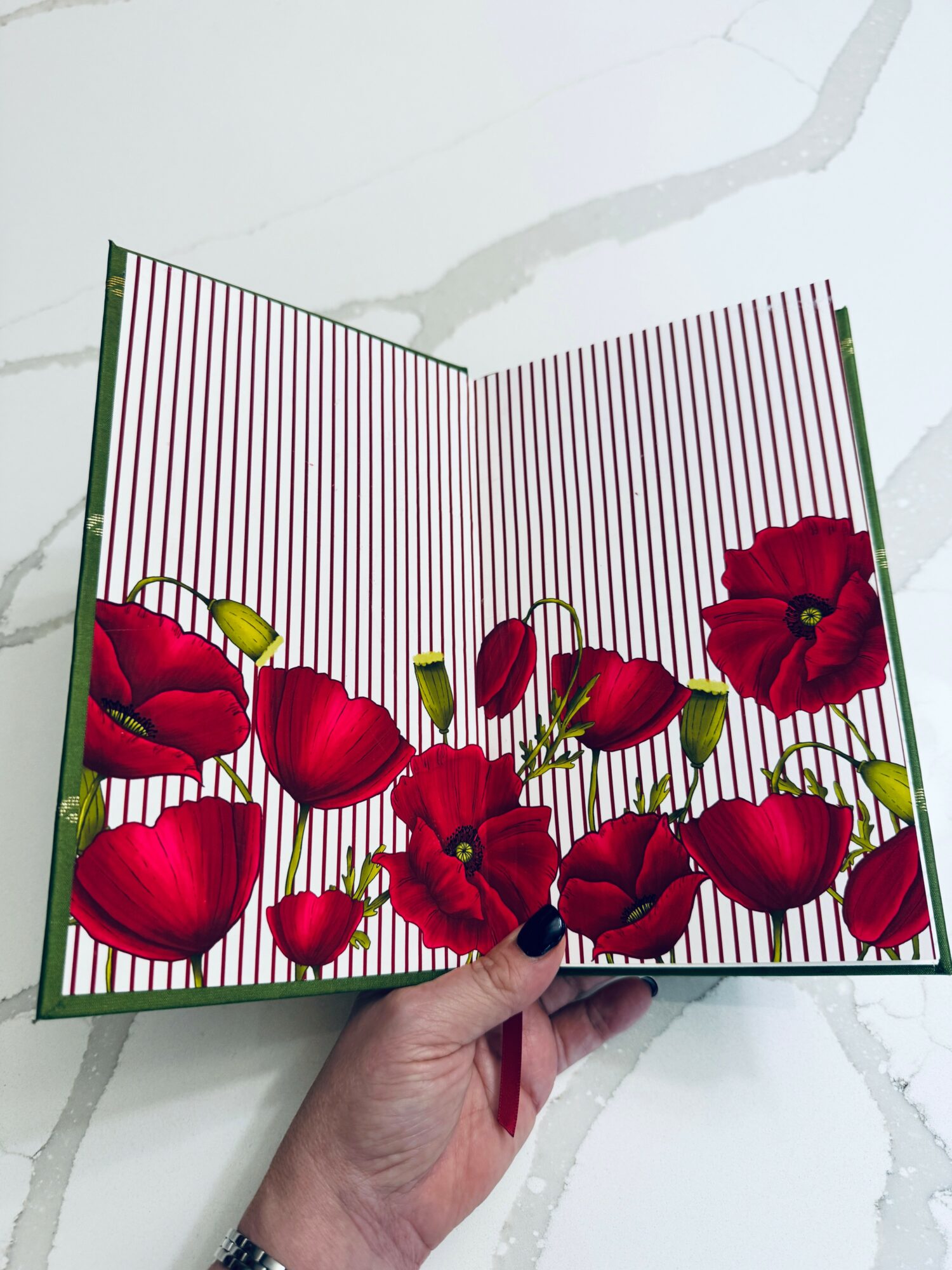 Open book with red poppy flowers and vertical red and white stripes inside, held over a white surface.