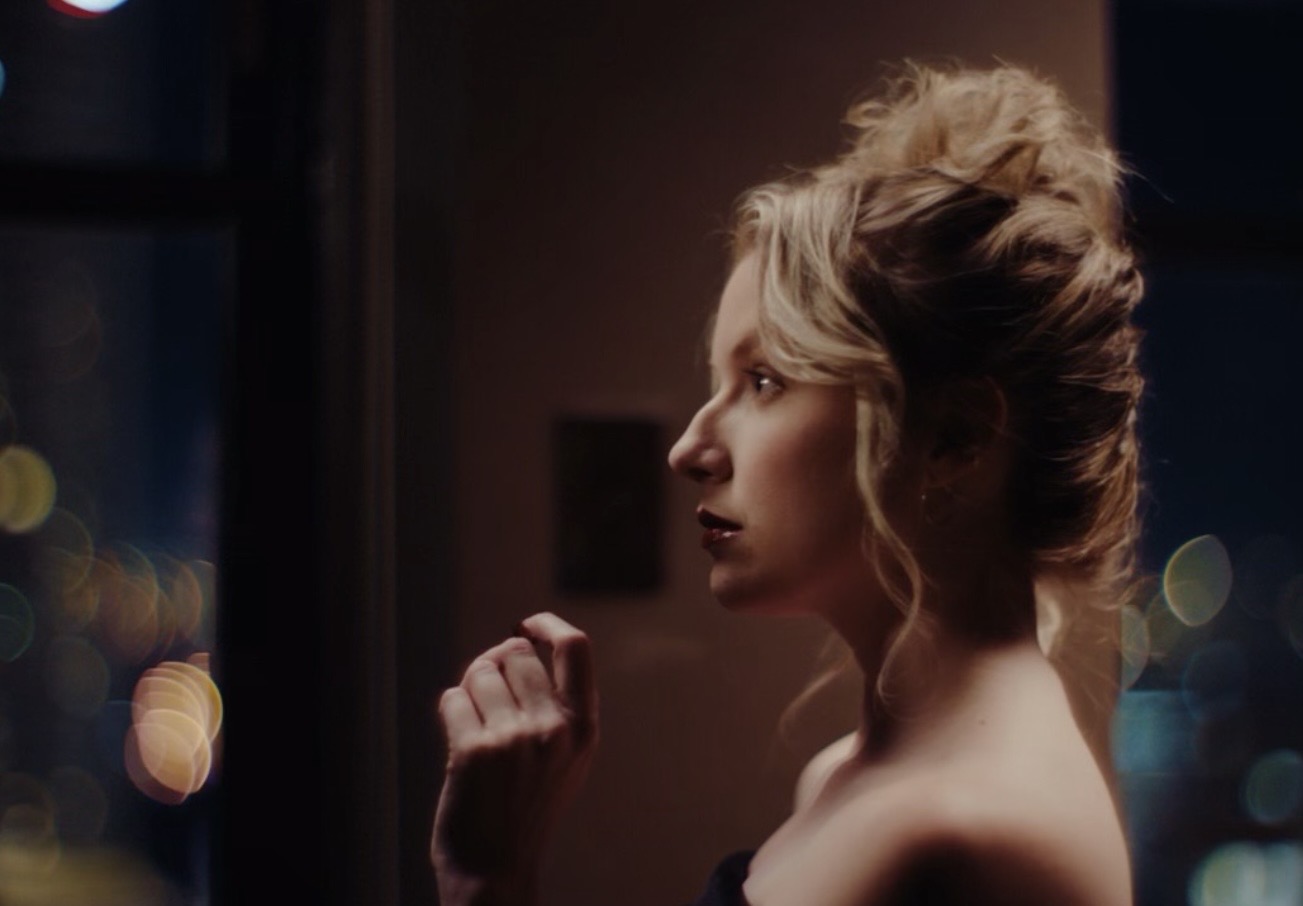 Profile of a woman with styled hair looking out a window at night, city lights blurred in background.