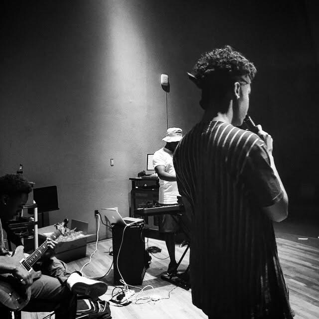 People practicing music in a dimly lit room with musical instruments and equipment.