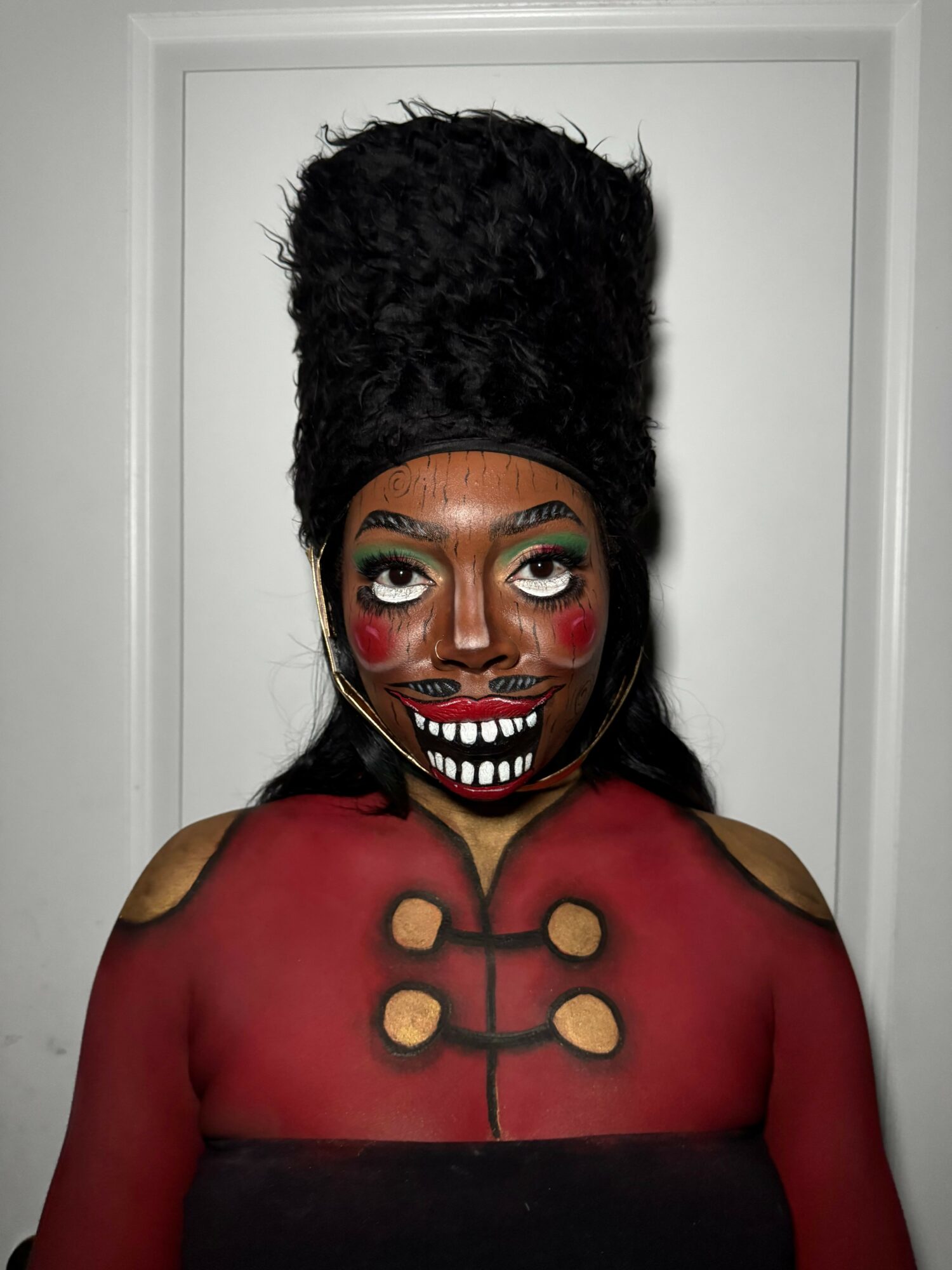 Person in clown makeup with a tall black hat, red and black costume, smiling face, and painted features.