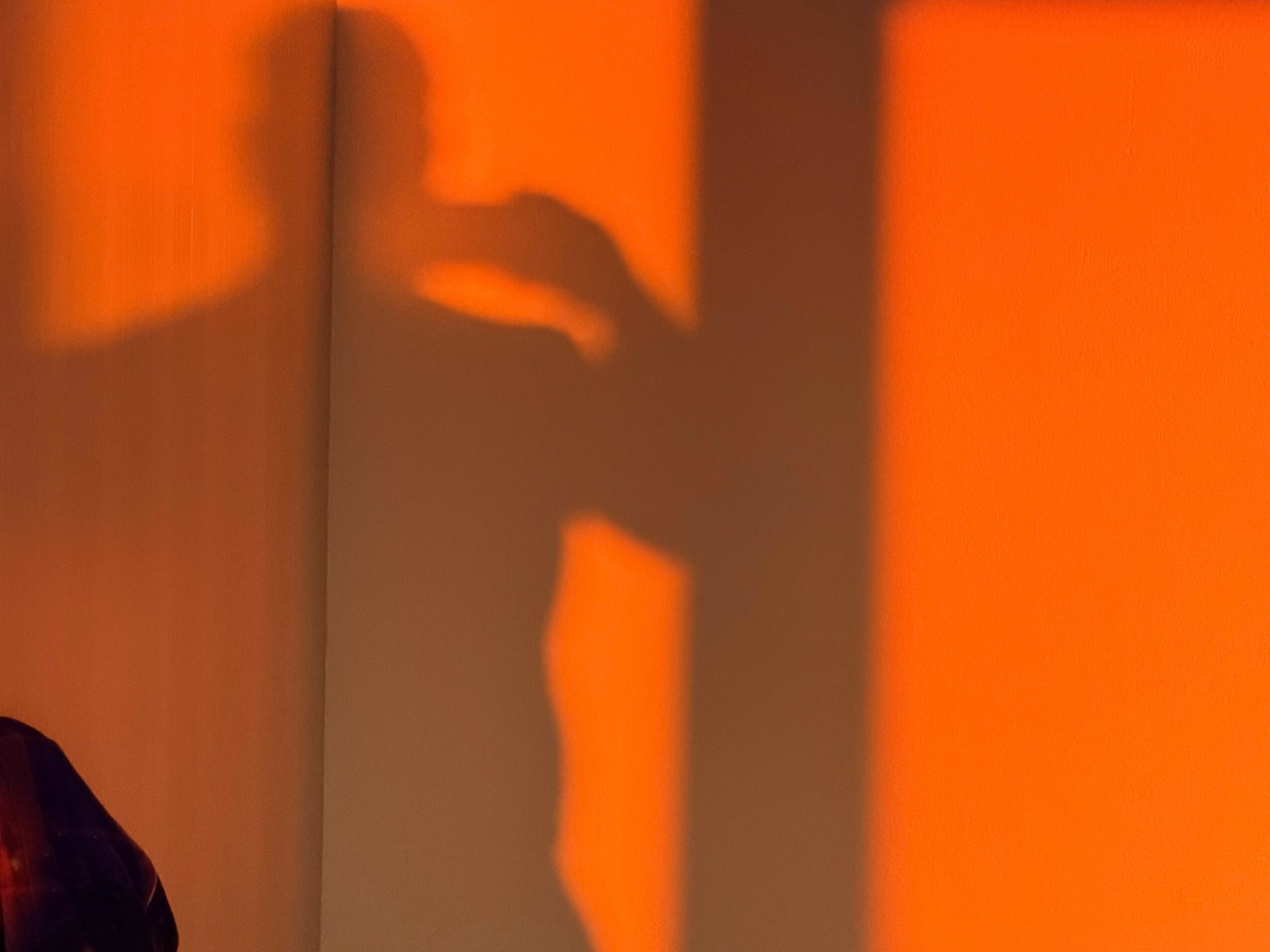 Shadow of a person reaching out with an arm, cast on an orange wall.