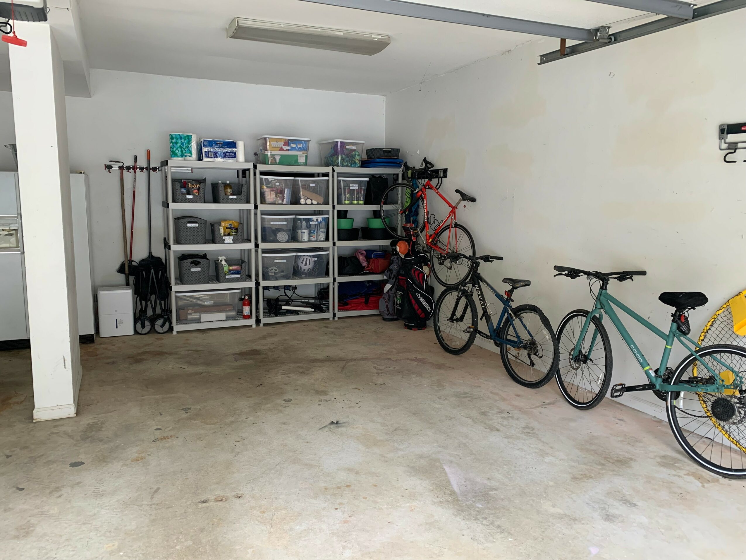 Garage with storage shelves, bicycles, and tools against the wall, concrete floor, white walls, ceiling light.