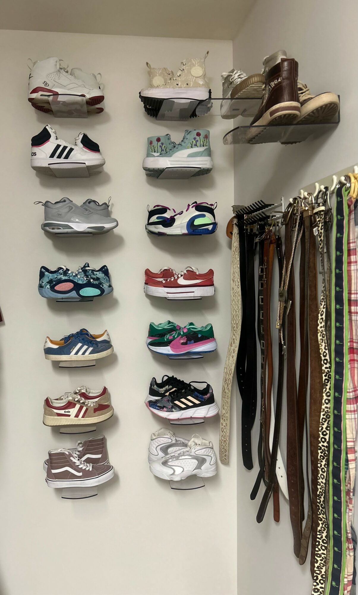 Wall display of various sneakers and boots, with belts hanging on the right side.