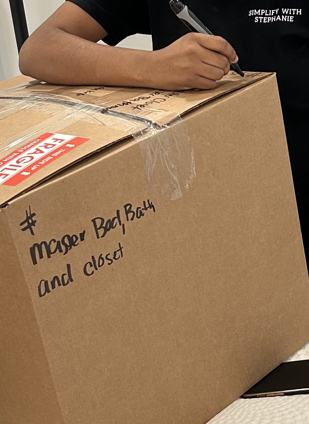 Person writing on a cardboard box labeled 'Manager Bad Boy and Closet' with a marker.