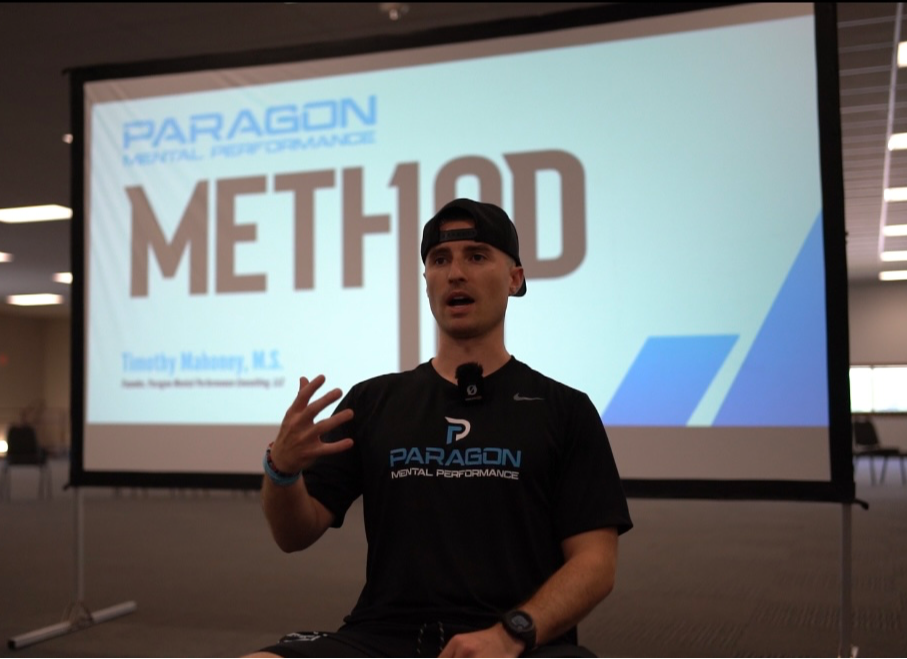 Person speaking in front of a presentation screen with 'METHOD' and 'PARAGON' logos, wearing a black shirt and cap.