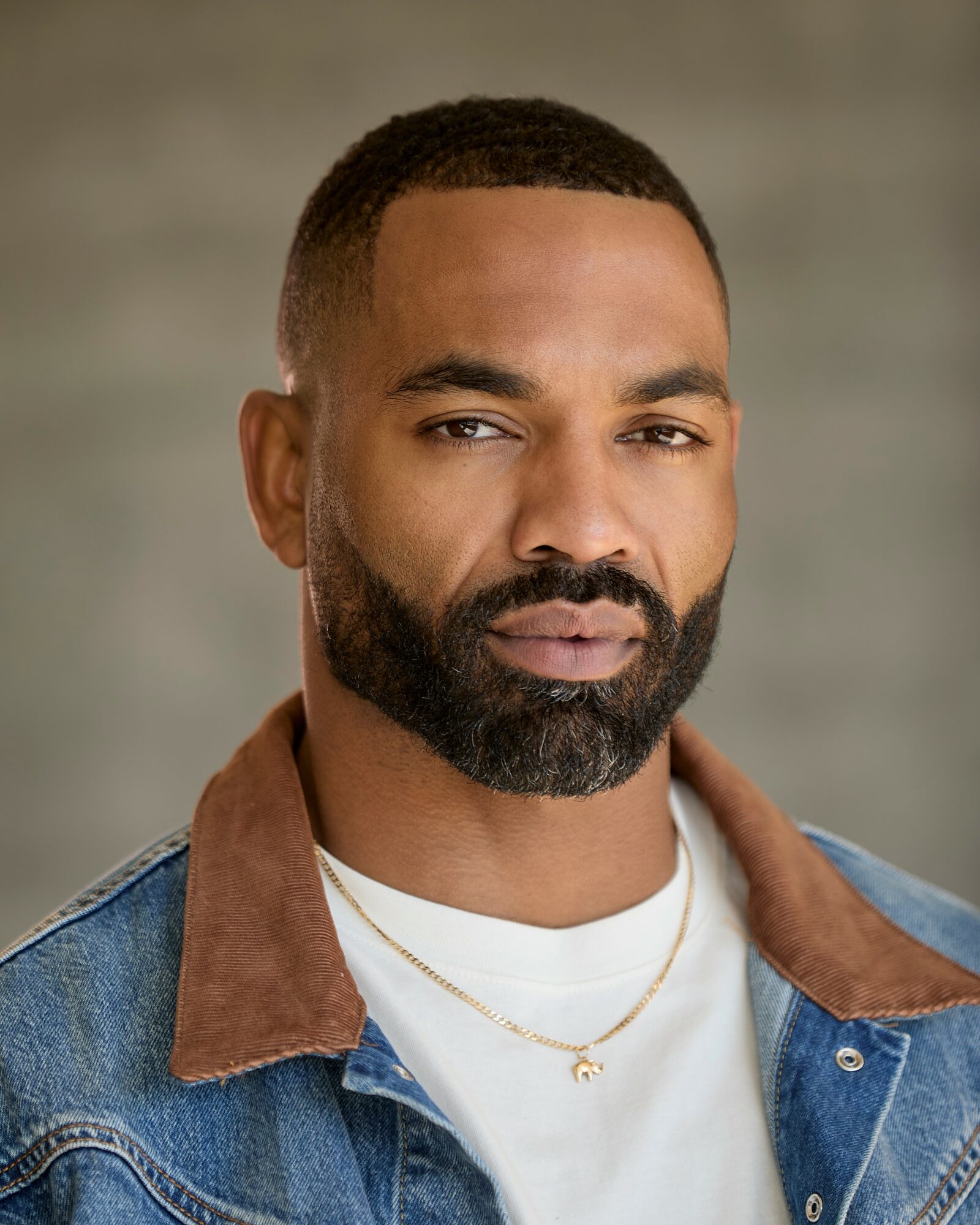 Man with short hair and beard wearing a denim jacket and white shirt, looking at the camera.